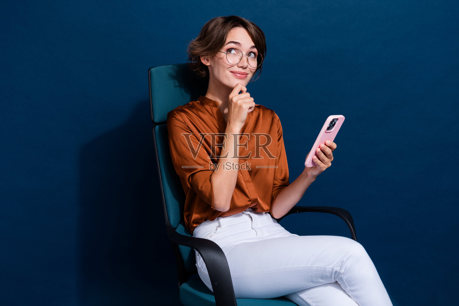 可爱的年轻女士的照片肖像小工具空的空间坐在扶手椅上穿时髦的棕色衬衫孤立在深蓝色的背景照片摄影图片