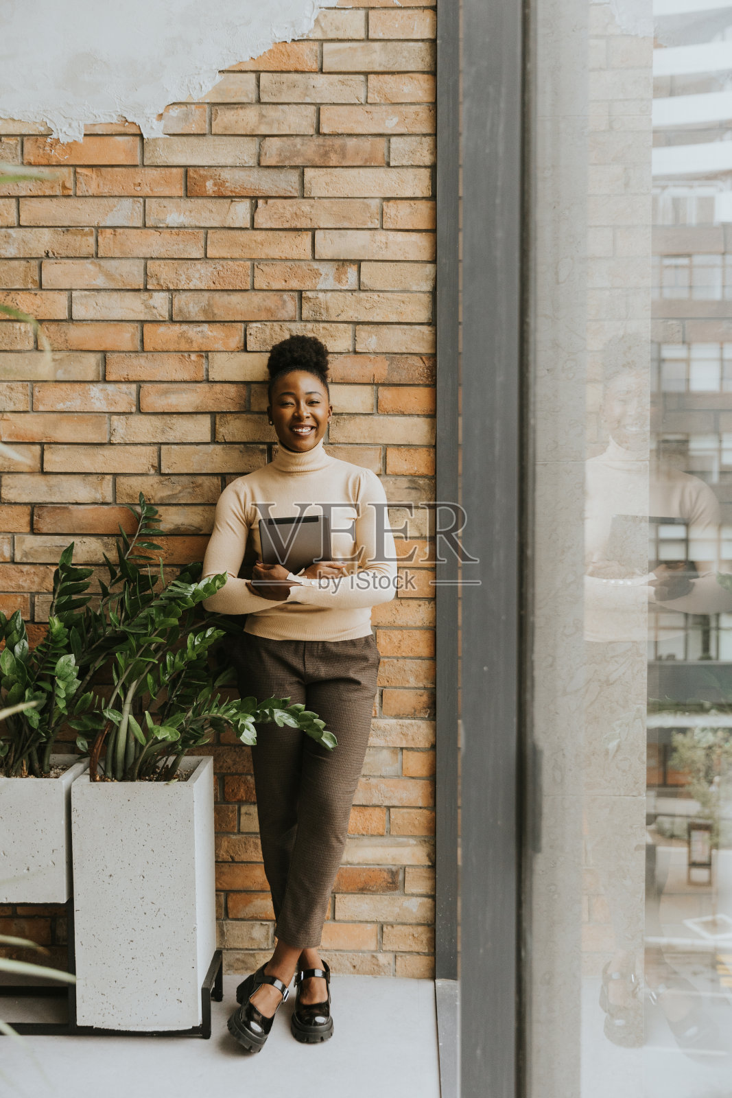 一位年轻的非裔美国女商人拿着数码平板电脑站在工业风格办公室的砖墙旁照片摄影图片