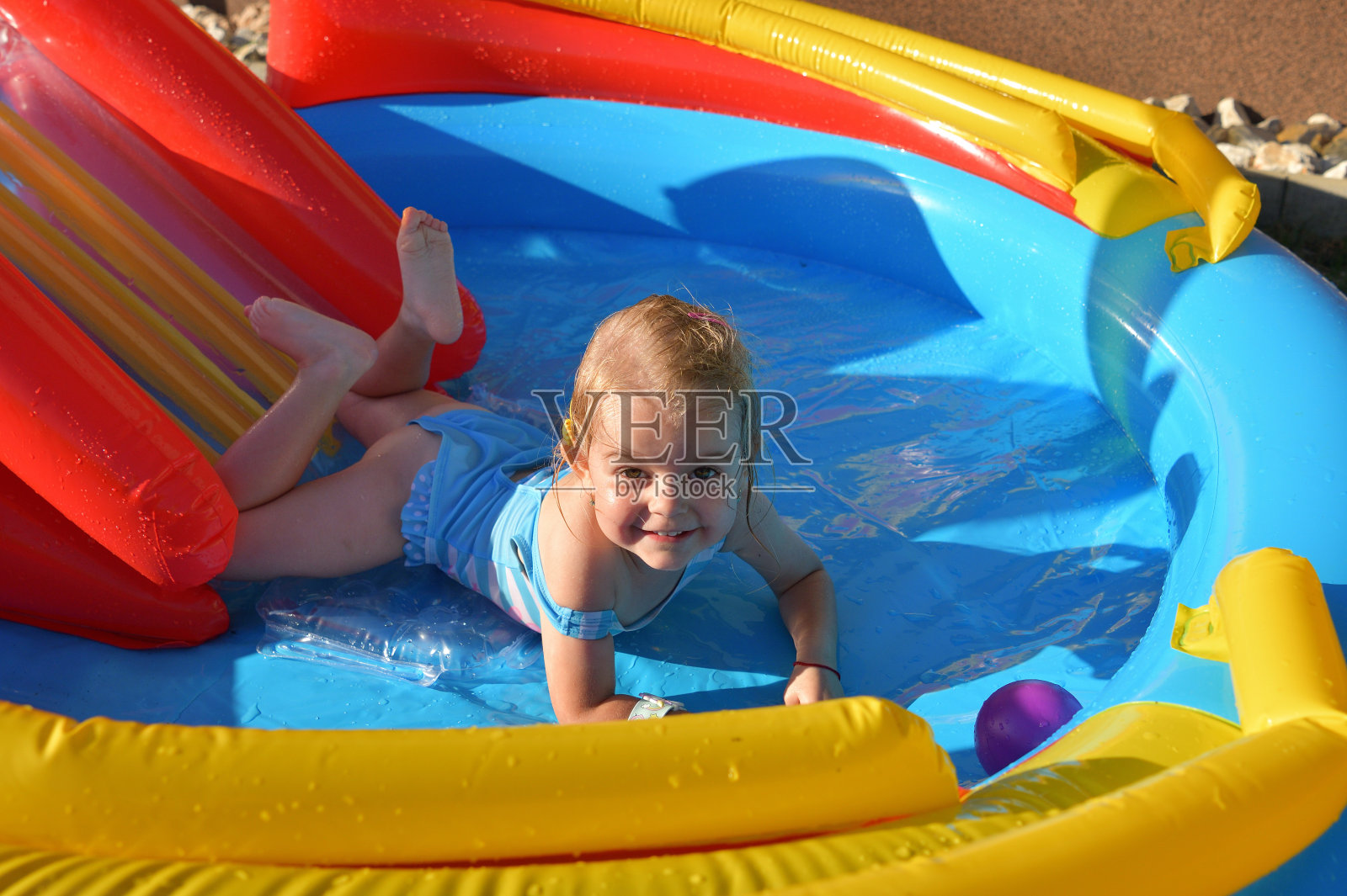 女孩在家里的充气游泳池里的水上滑梯上滑行照片摄影图片