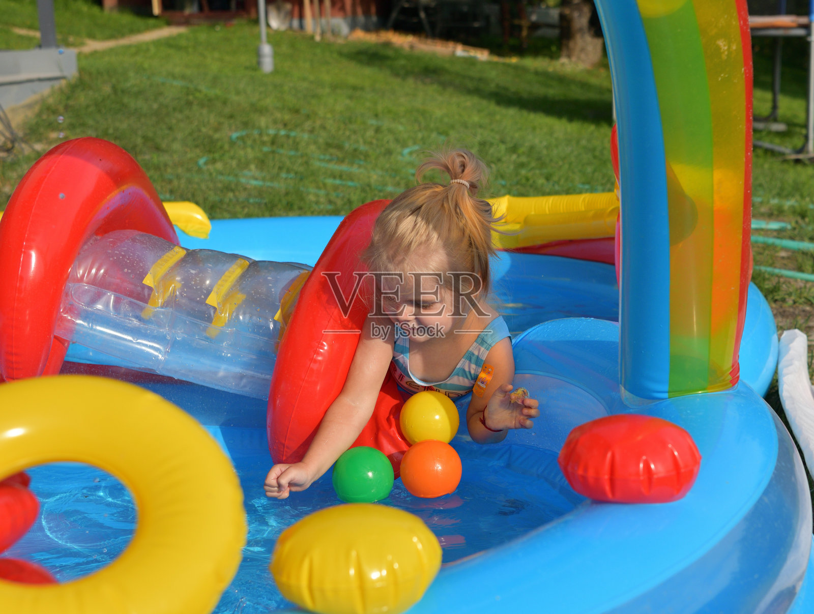 在一个炎热的夏天，一个小女孩在家里游泳池的水滑梯上滑行照片摄影图片