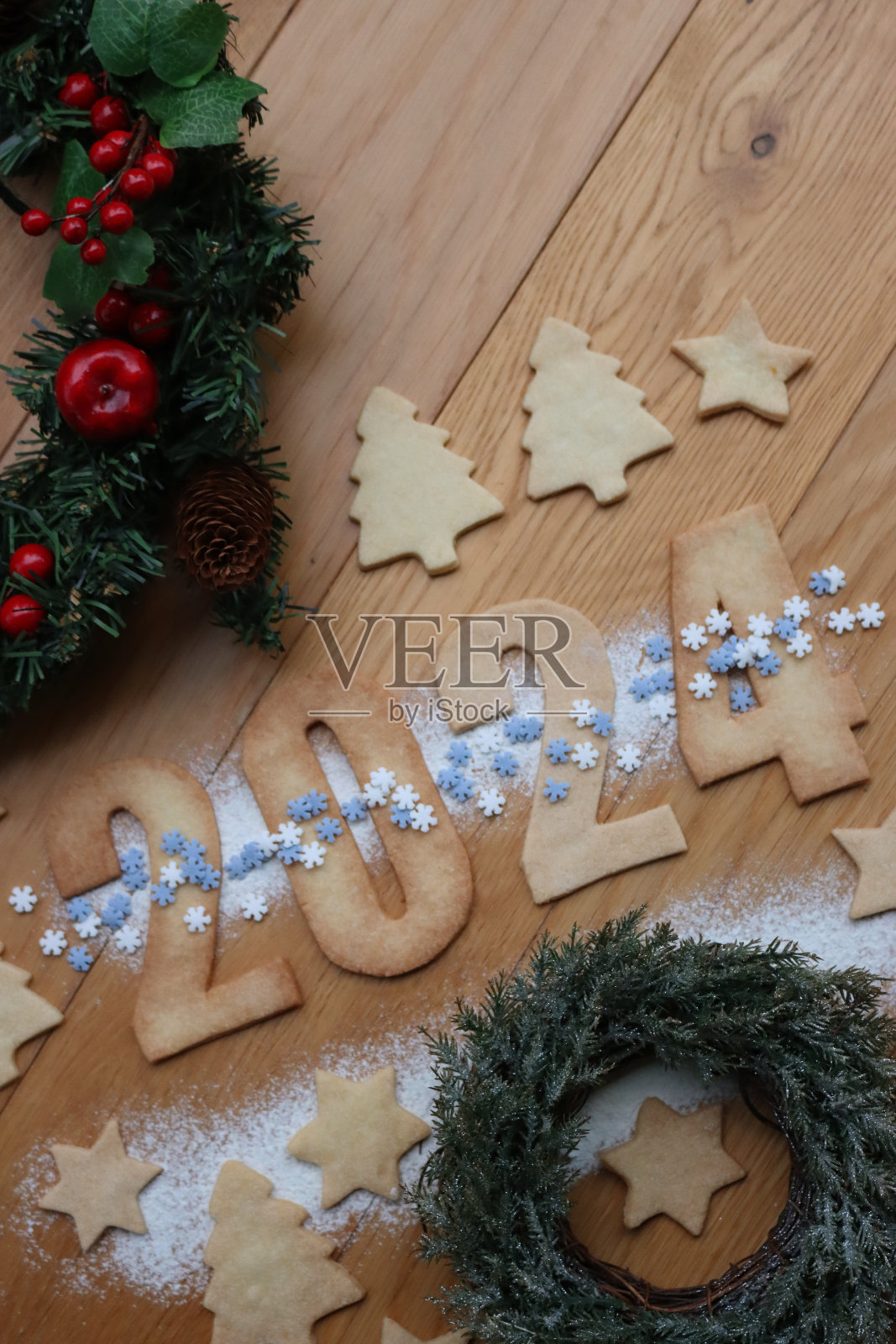 饼干上撒着数字2024形状的雪花，桌上放着松木花环和装饰品照片摄影图片