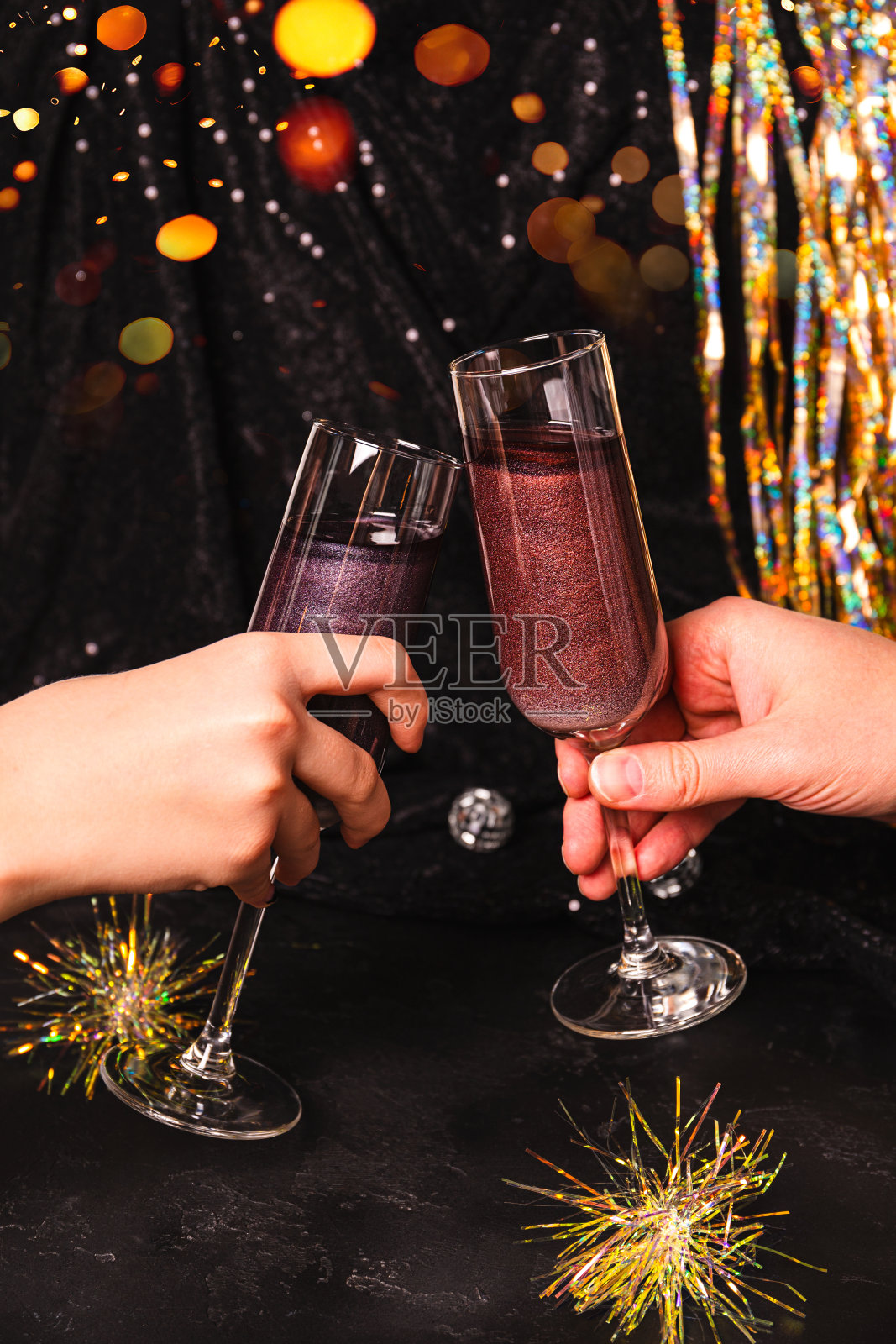 手拿着新年鸡尾酒的酒杯，上面有可食用的闪光，在圣诞彩灯中张望照片摄影图片