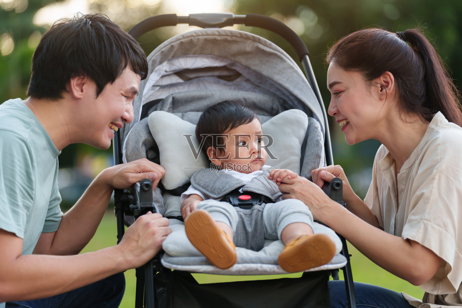 快乐的父母(爸爸和妈妈)在公园休息时与婴儿车里的婴儿交谈和玩耍照片摄影图片
