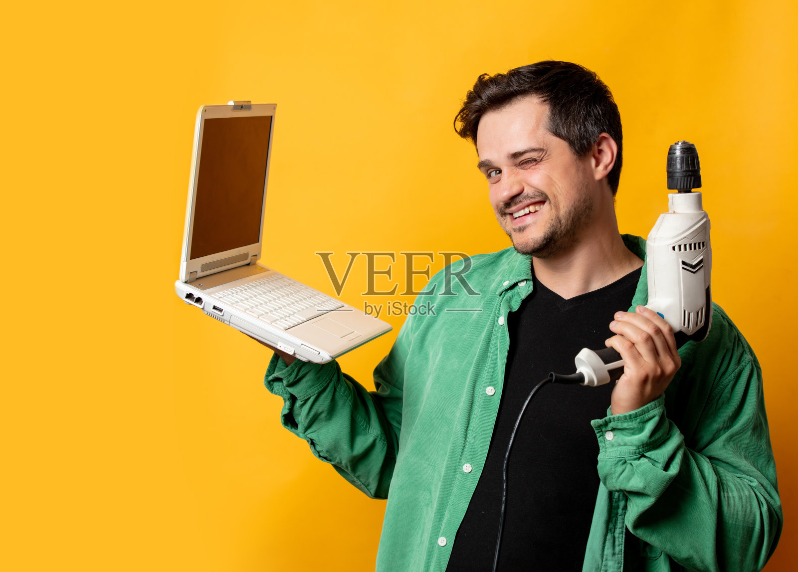 穿着绿色衬衫，带着电钻和笔记本电脑的时髦男人照片摄影图片