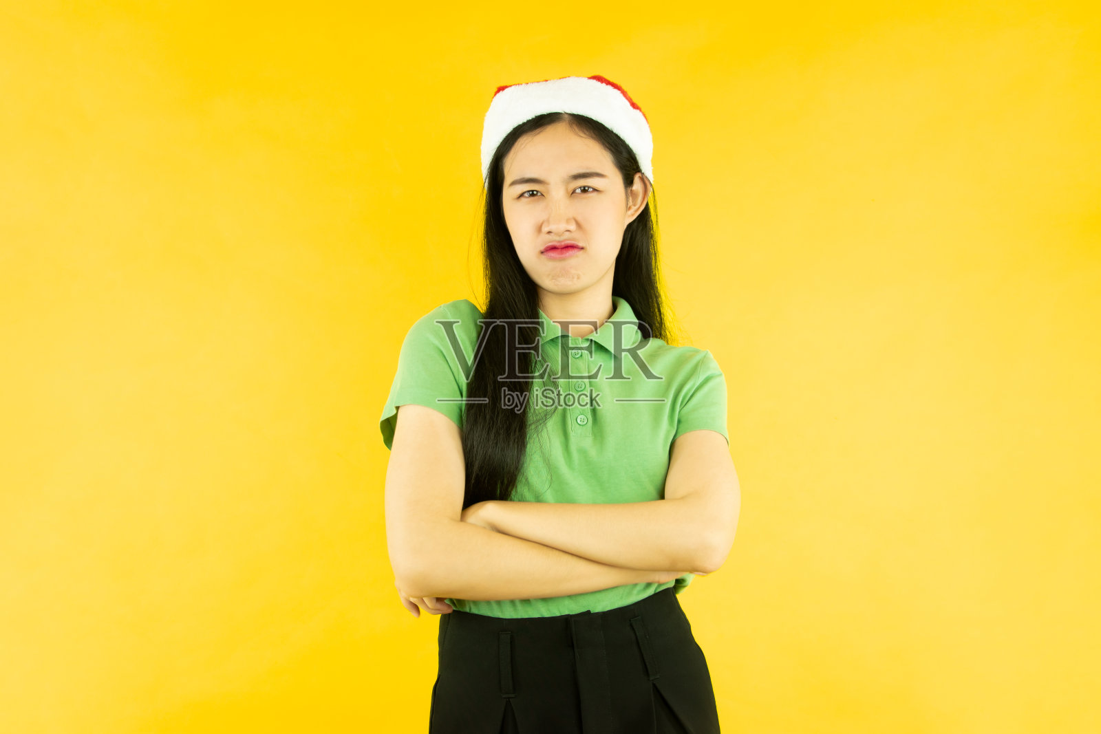 画像中亚洲女子头戴红色圣诞老人帽，背景孤立黄色，圣诞概念照片摄影图片