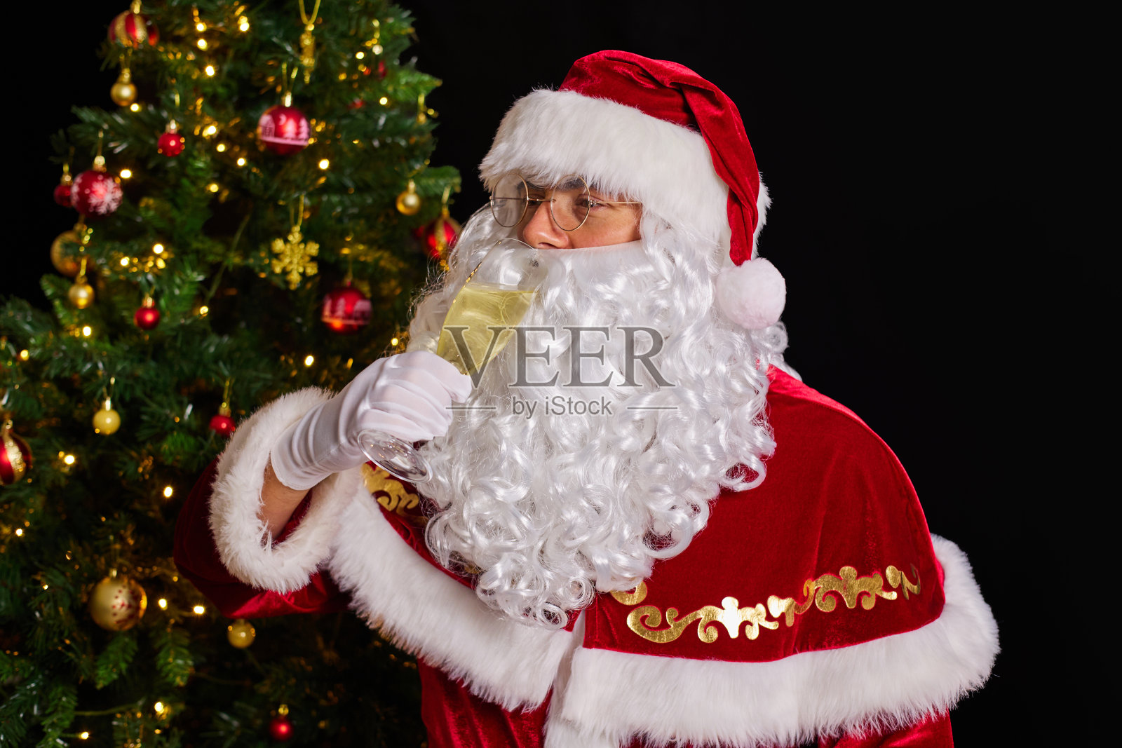 圣诞老人在圣诞树的背景下喝着一杯香槟照片摄影图片