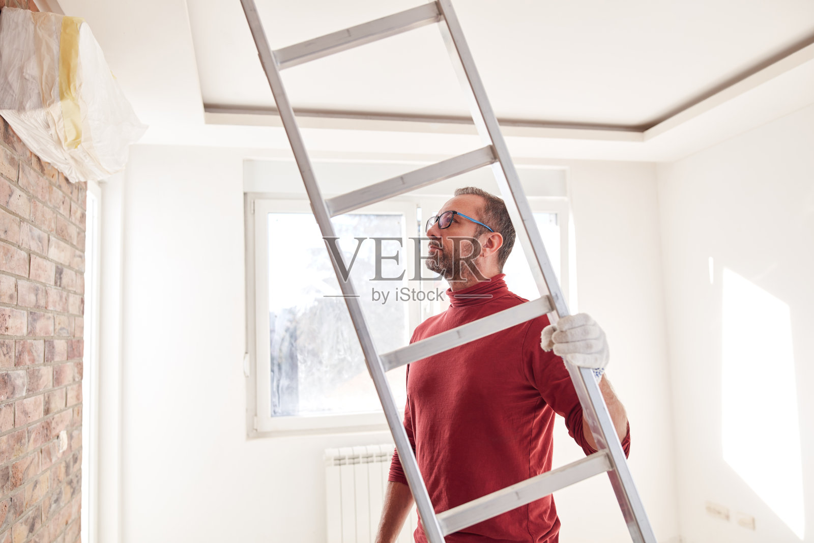 在新房内部用梯子工作的勤杂工电工。照片摄影图片