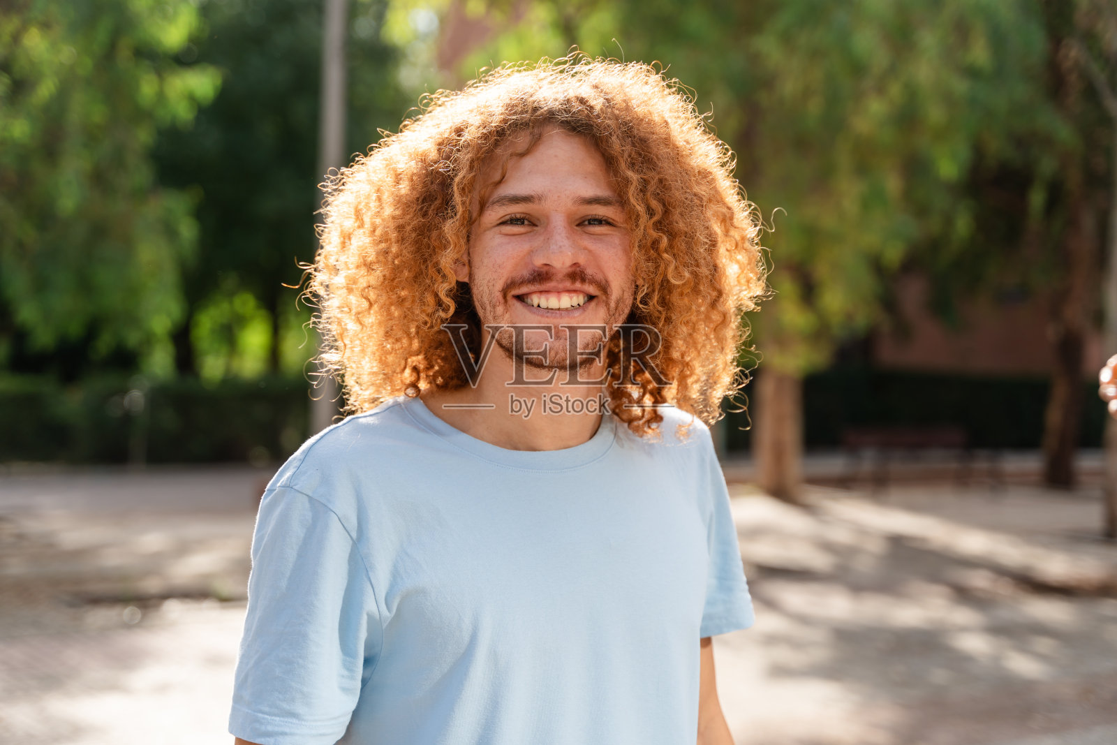 一个开朗的卷发年轻人站在公园里的画像照片摄影图片