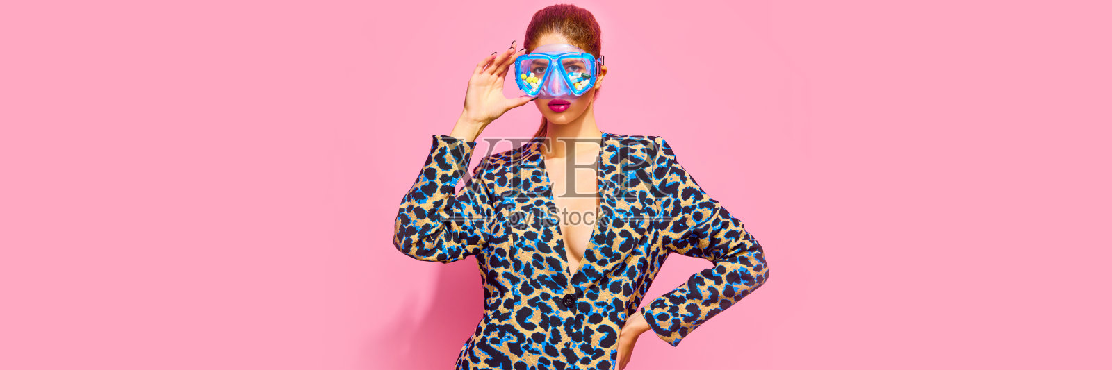 横幅。迷人的女士穿着优雅的动物印花布，在游泳面具上布满药丸、维生素片、孤立的粉红色背景。照片摄影图片