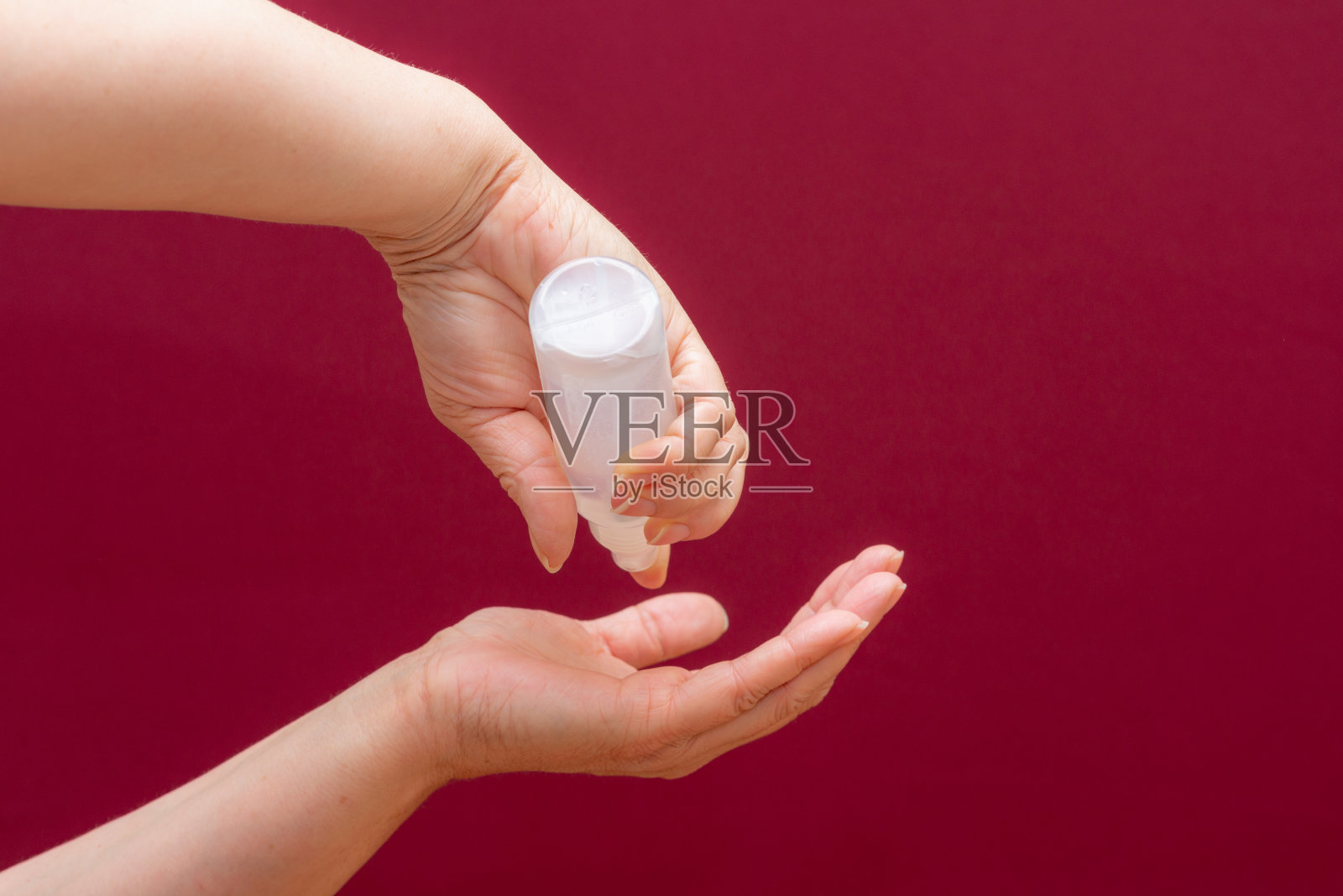 手握抗菌消毒剂酒红色背景。冠状病毒防护概念。照片摄影图片