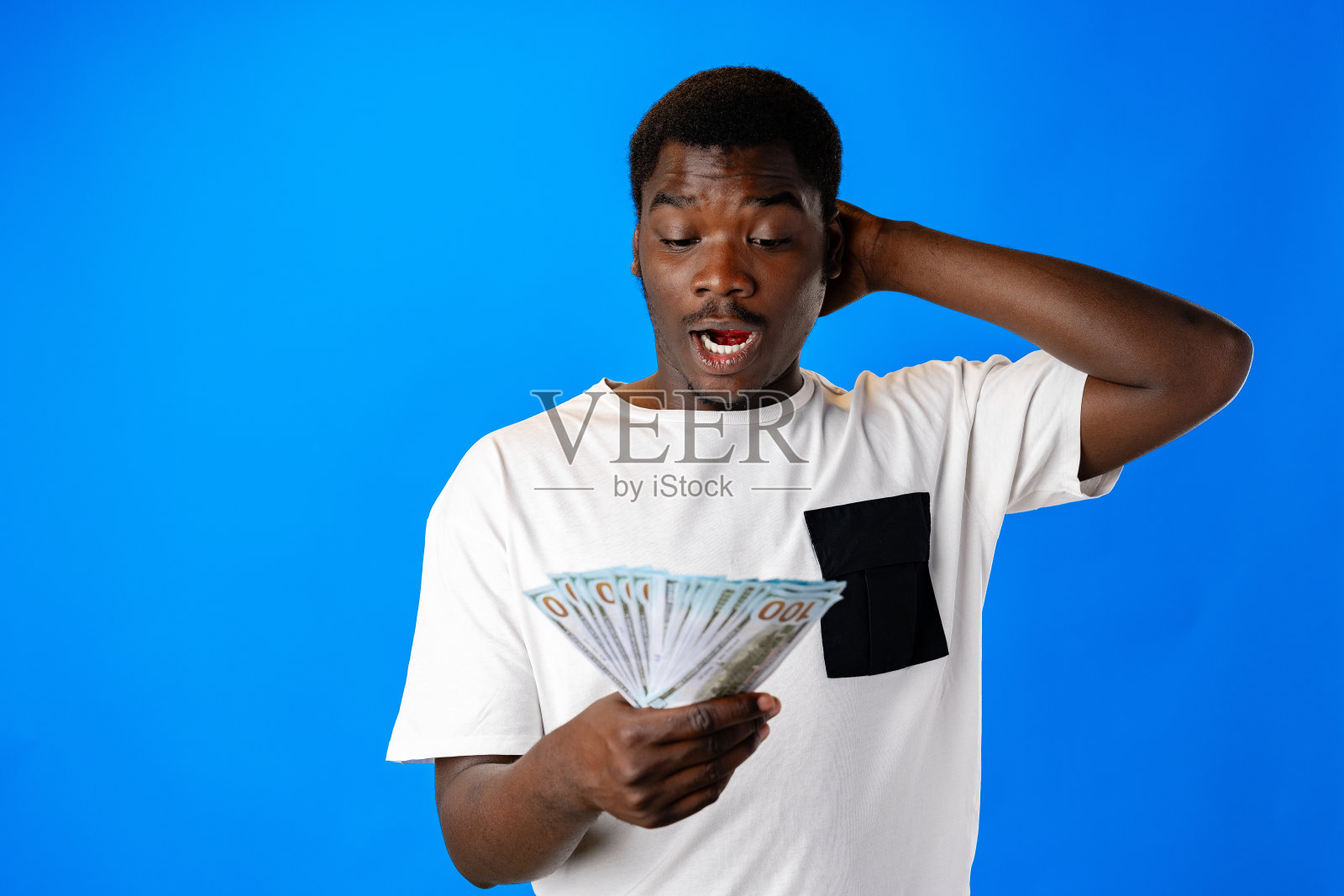 年轻的非洲男子手里拿着蓝色背景的美元钞票照片摄影图片
