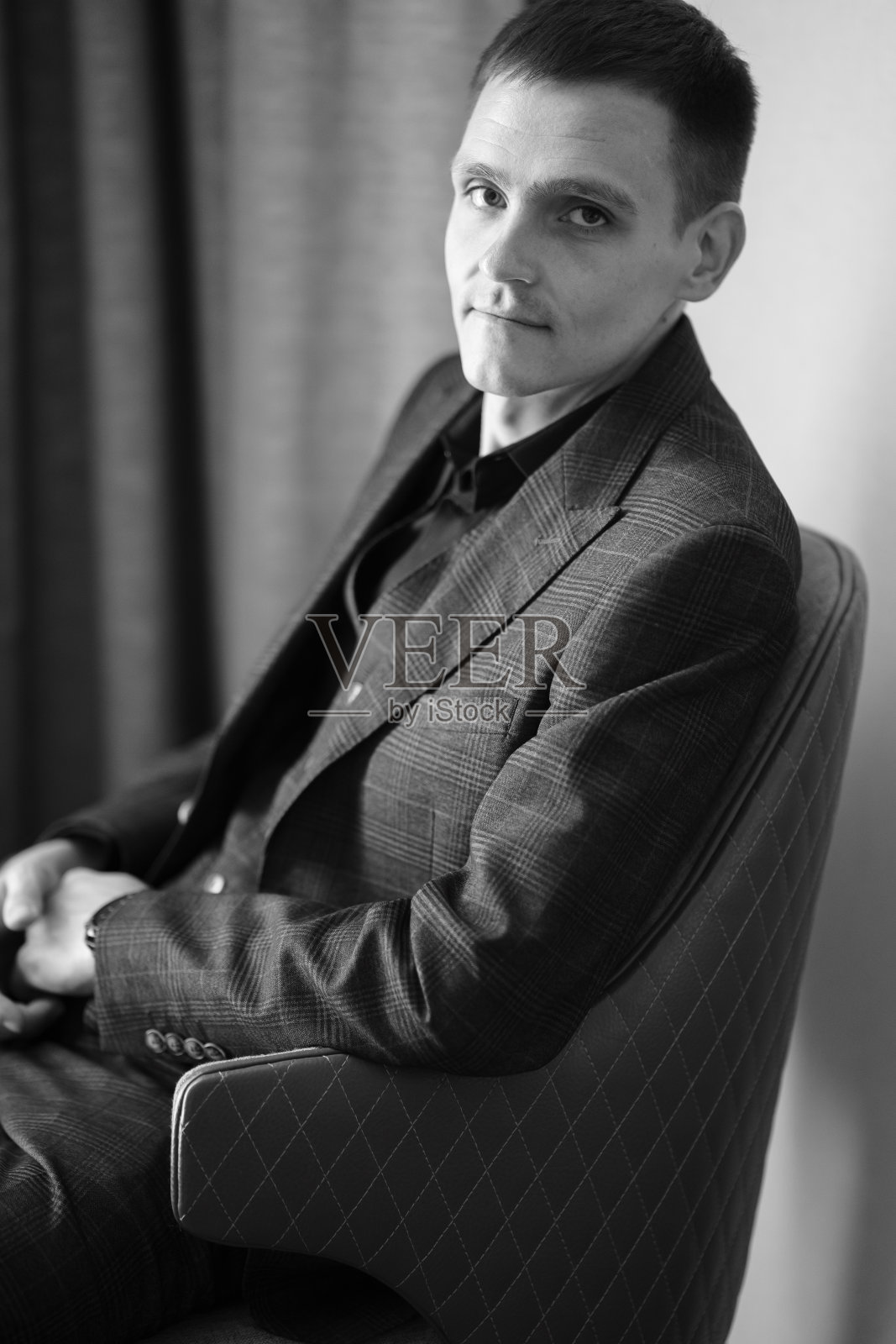 一个穿着格子西装的年轻人坐在椅子上的画像。商业肖像。照片摄影图片