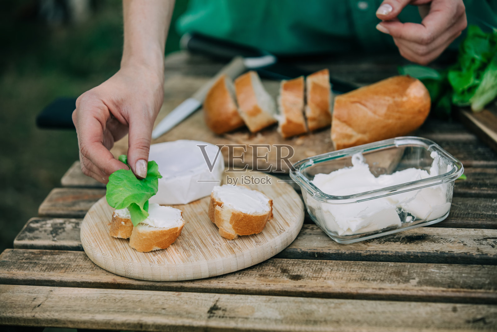 穿着绿色衬衫的时髦女子在户外的桌子上用面包和奶酪做点心照片摄影图片