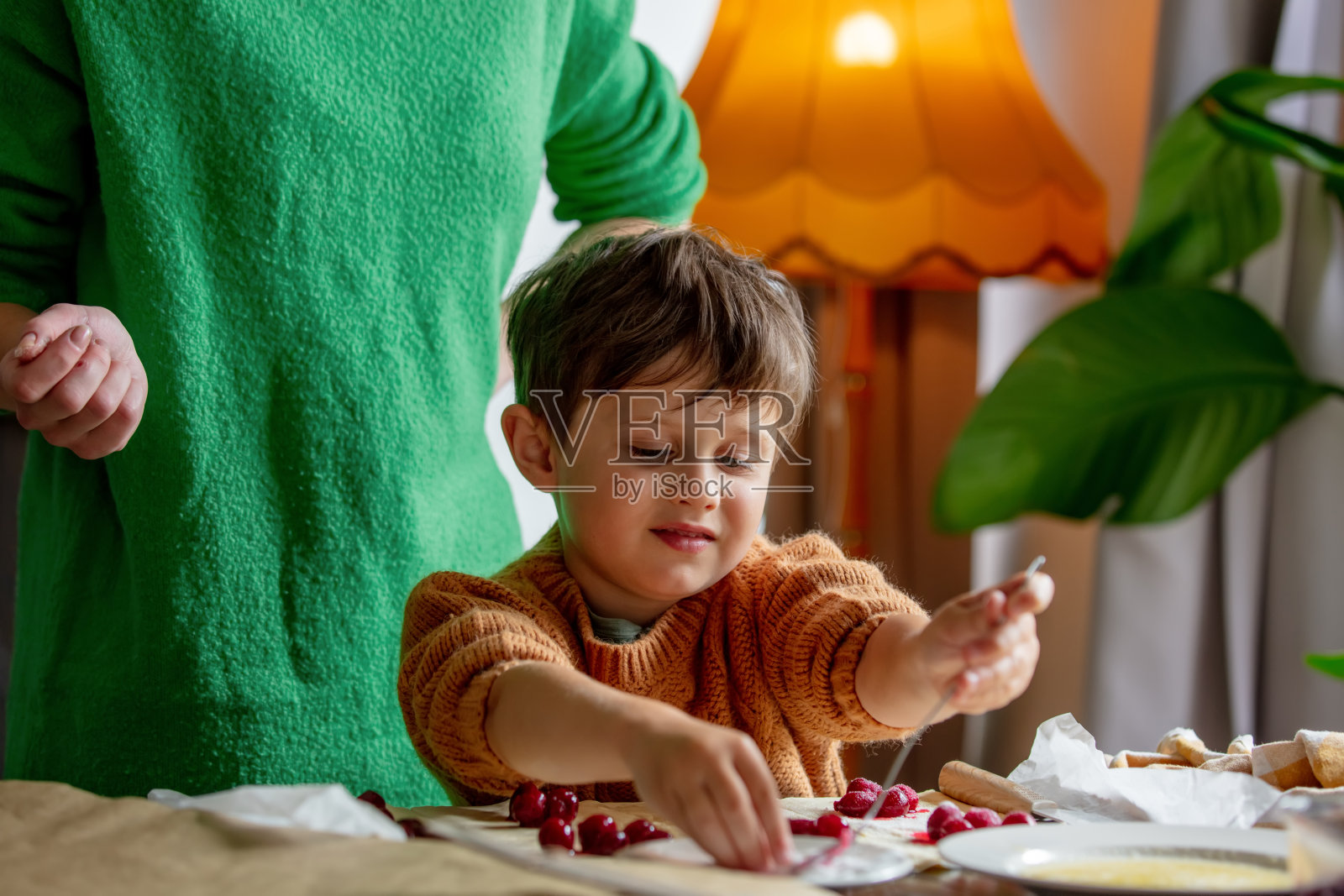 母亲带着儿子在家用樱桃做饼干。照片摄影图片