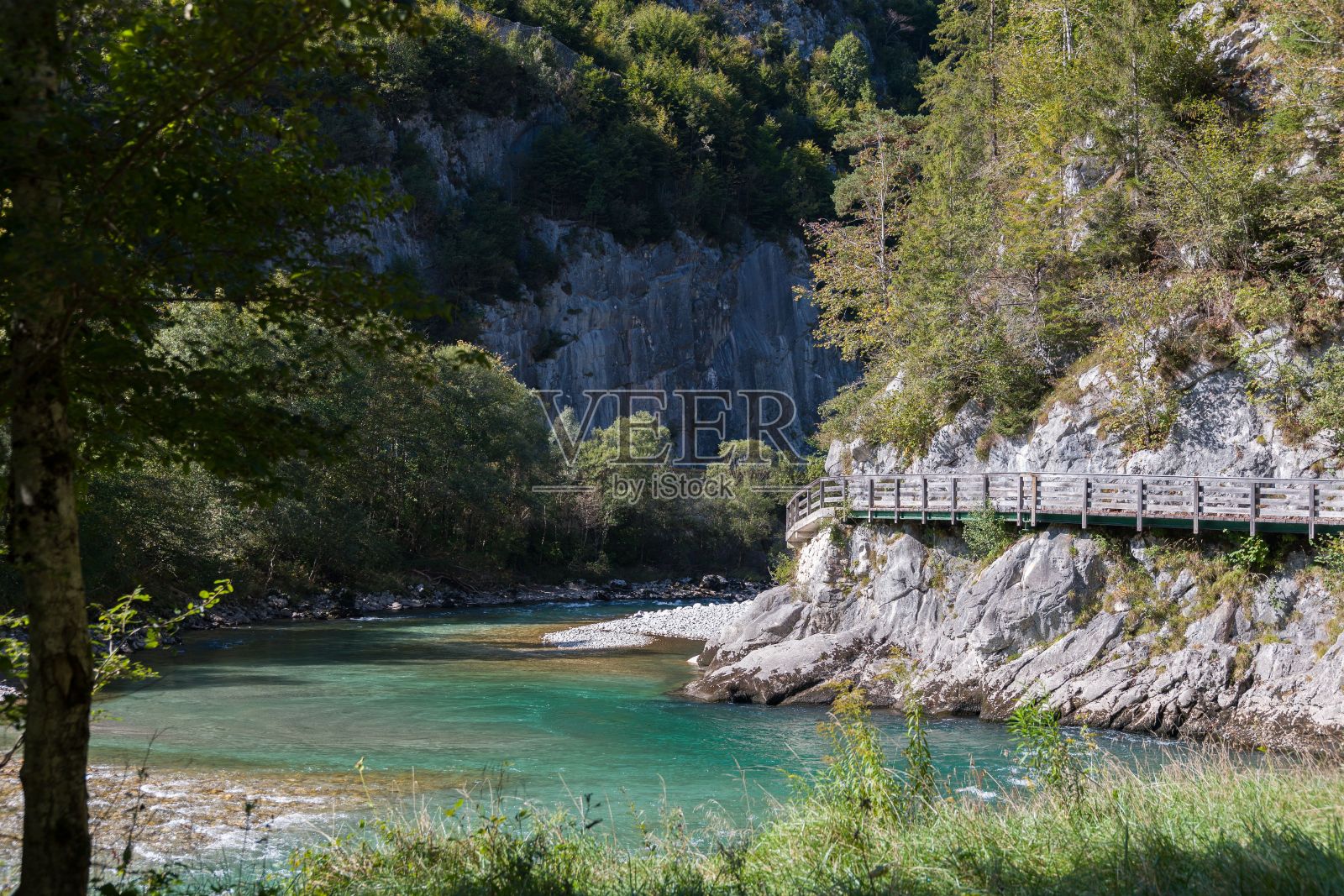 一座木桥，通向位于岩石悬崖前的河流照片摄影图片