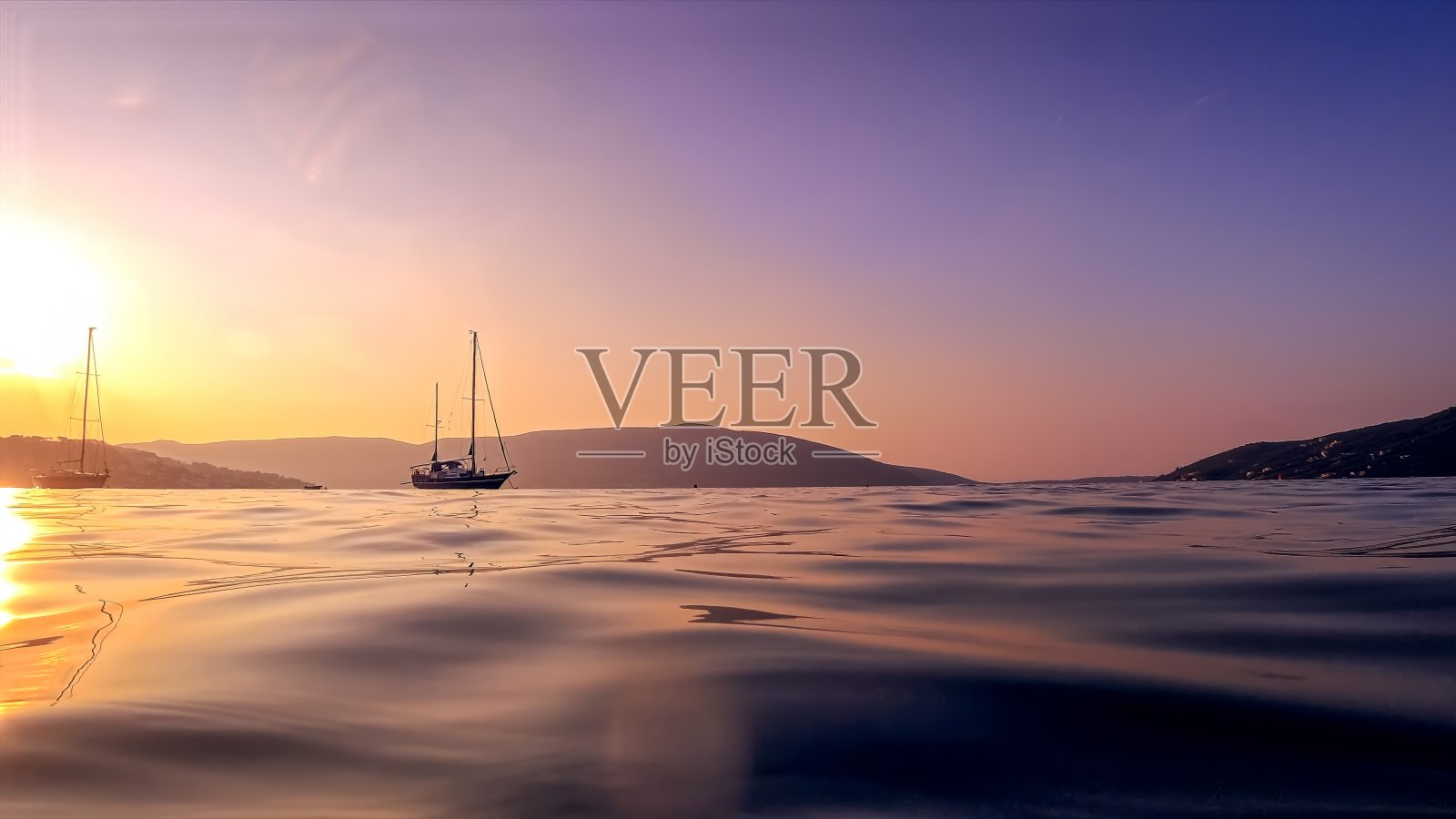 一艘游艇的剪影在夕阳的天空和山脉的背景下，从宁静的海面照片摄影图片