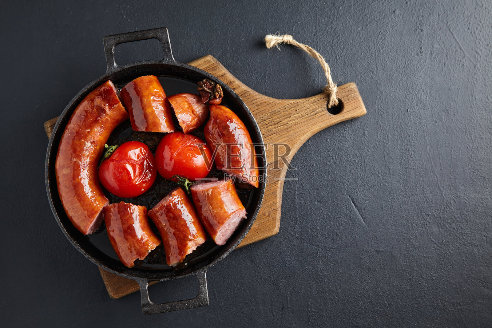 在黑色的混凝土桌子上，用铸铁煎锅煎猪肉香肠，烤西红柿。带复制空间的俯视图照片摄影图片