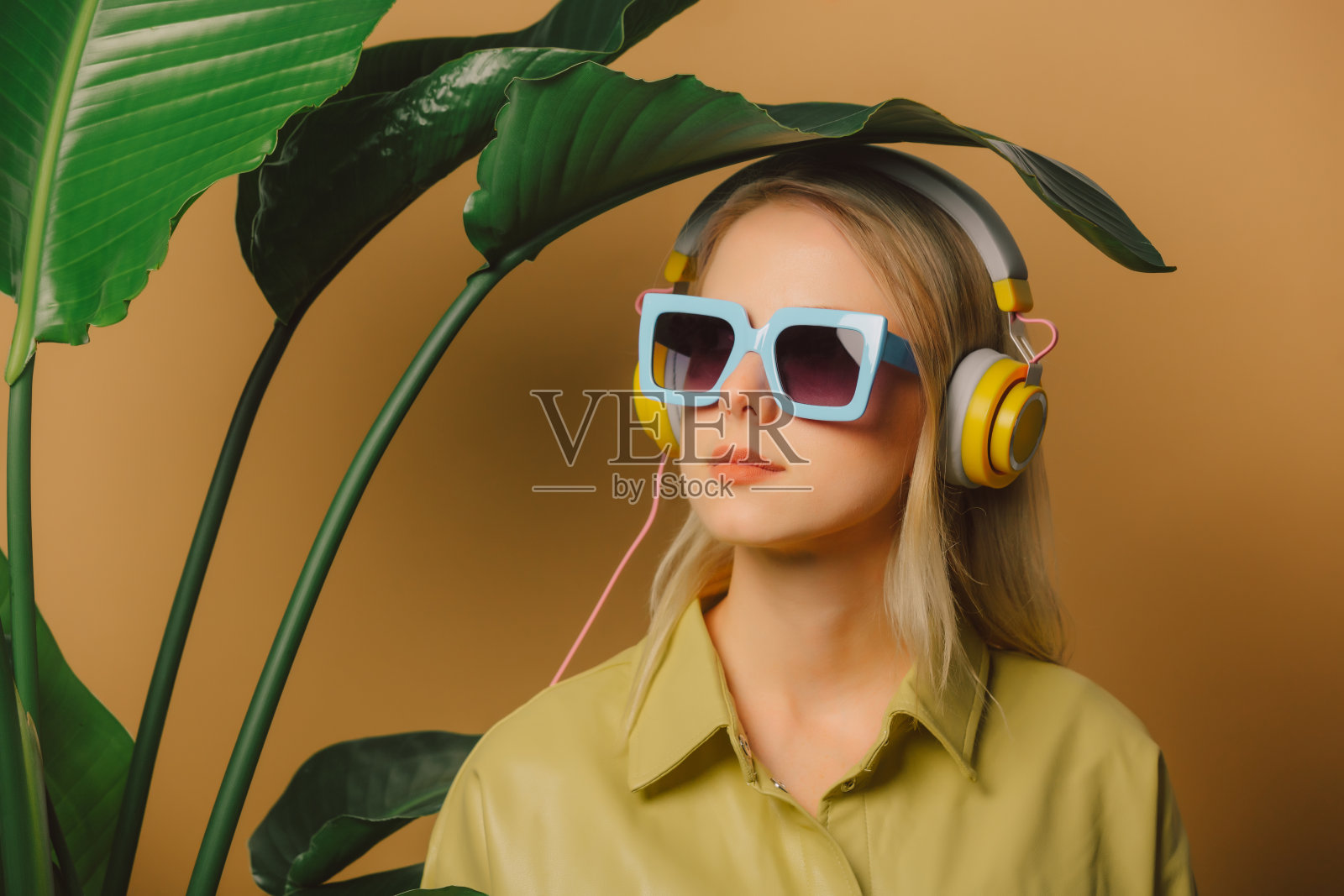 80年代的时髦女人戴着眼镜和耳机，在棕色背景的棕榈叶下照片摄影图片