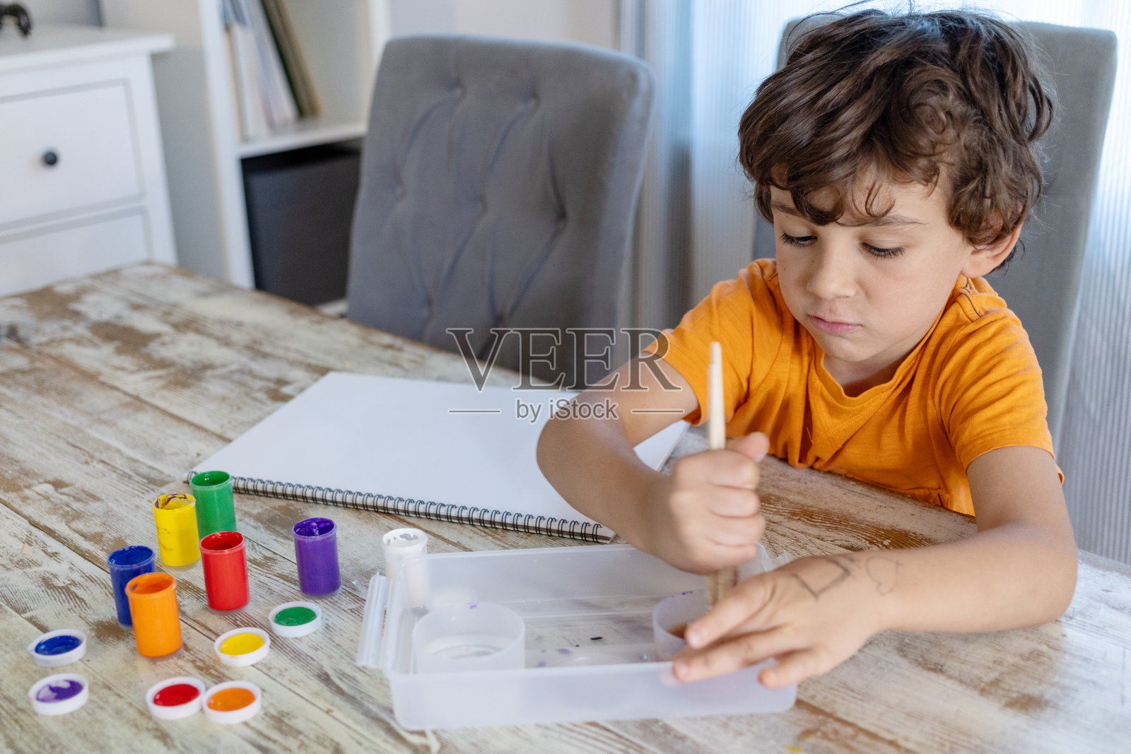 在清晨的阳光下，一位七岁的卷发小男孩勤奋地坐在家里的饭桌旁，在去上学前做作业照片摄影图片