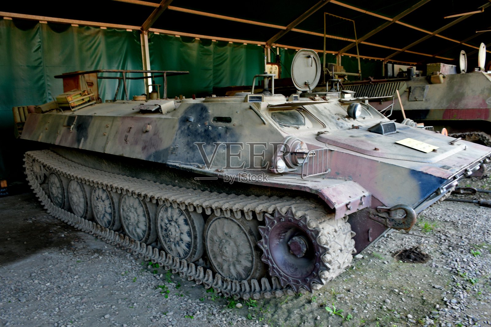 一辆废弃的旧军用卡车、坦克或运输车的特写镜头，由金属制成，车轮上有生锈的履带，在一条泥泞的小路上，旁边是一些原木、木材、备件和森林照片摄影图片