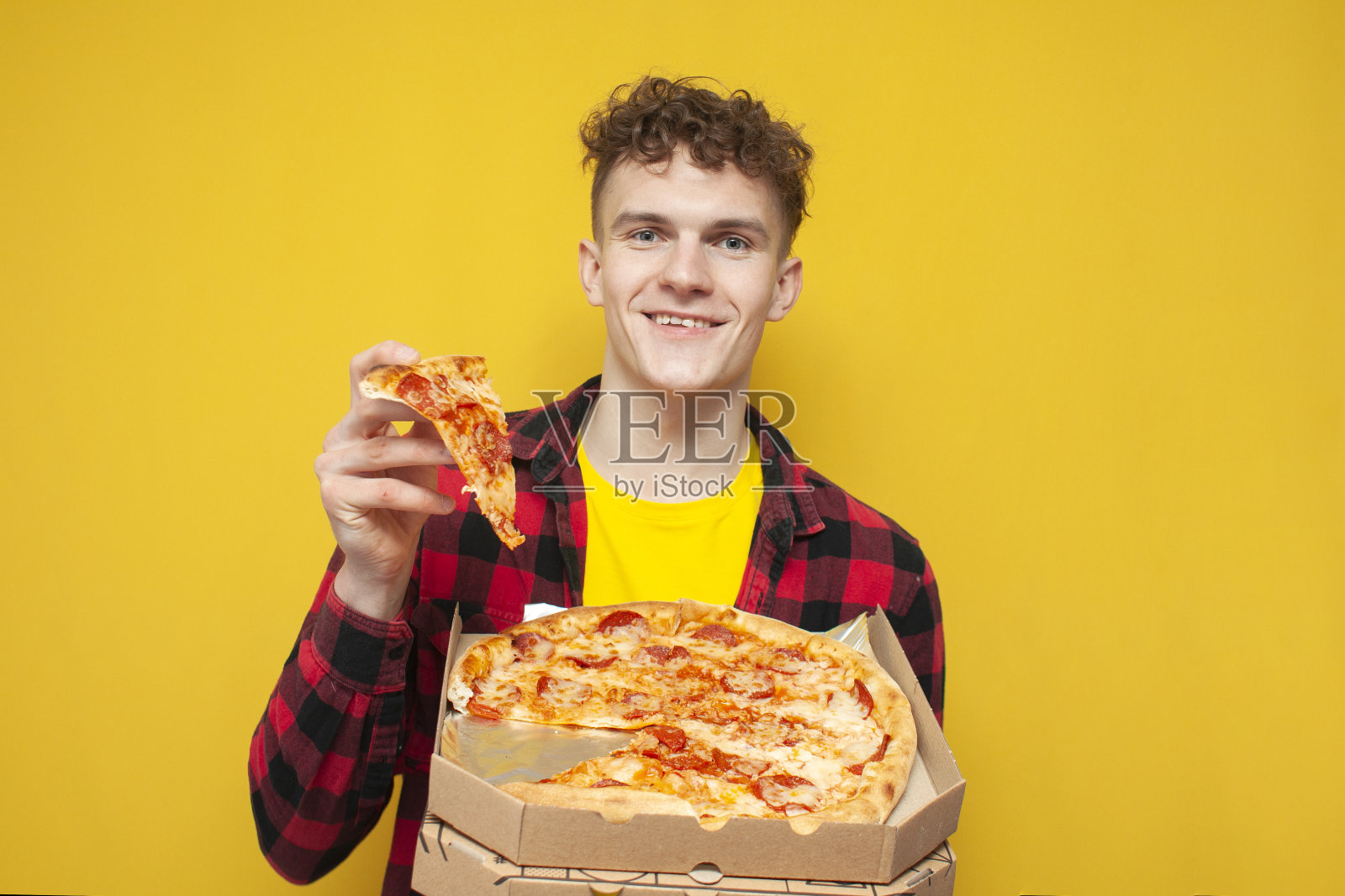 学生在黄色背景上吃披萨，卷毛男人在做快餐广告，微笑着照片摄影图片