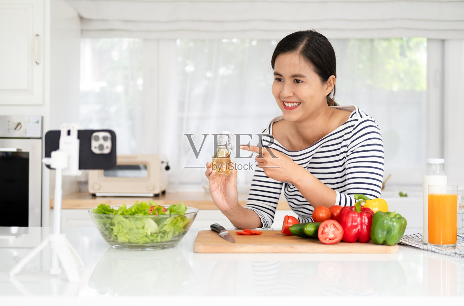 年轻女性视频博主在厨房烹饪沙拉健康食品并拍摄照片摄影图片