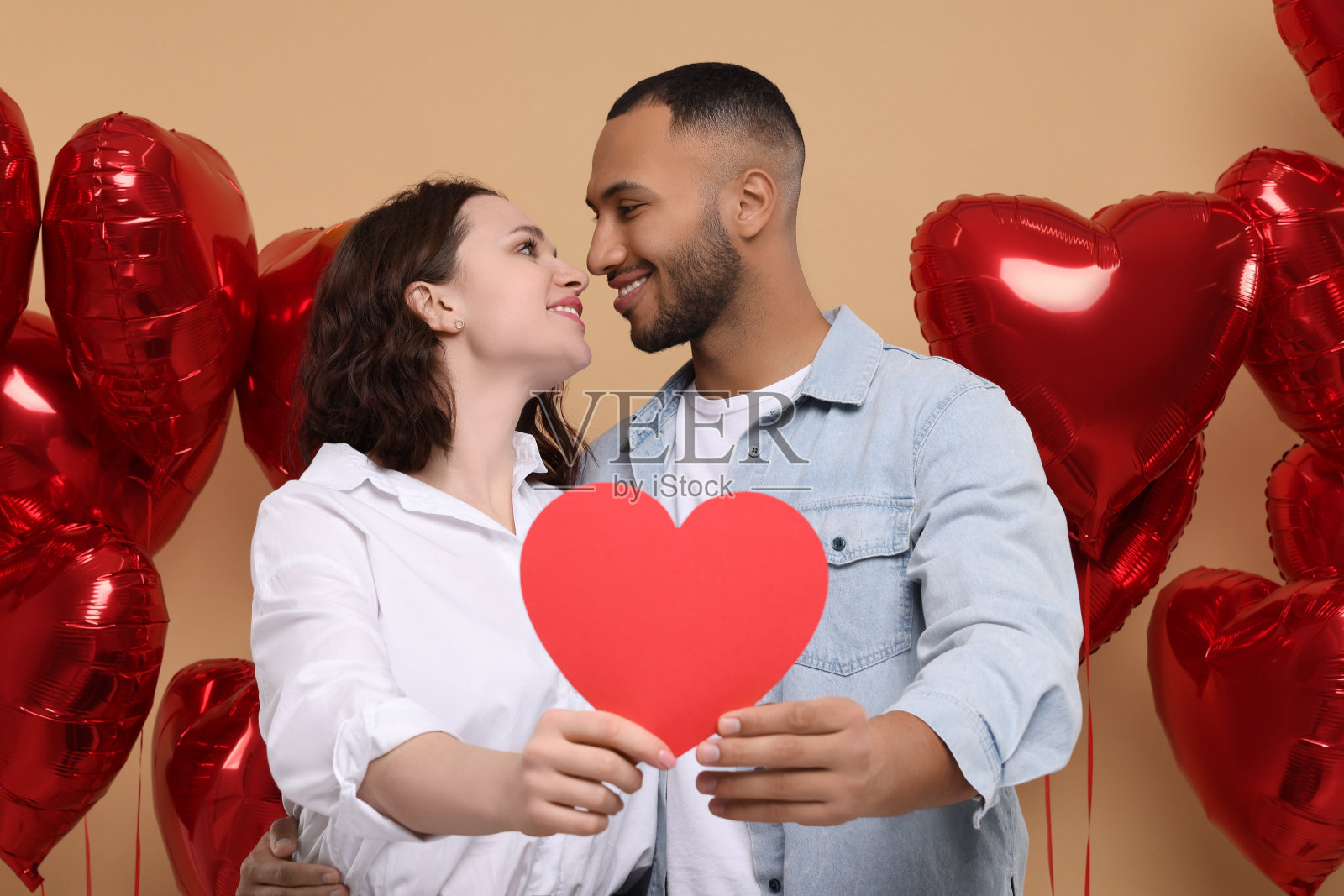 可爱的夫妇与红纸心形米色的背景。情人节庆祝活动照片摄影图片