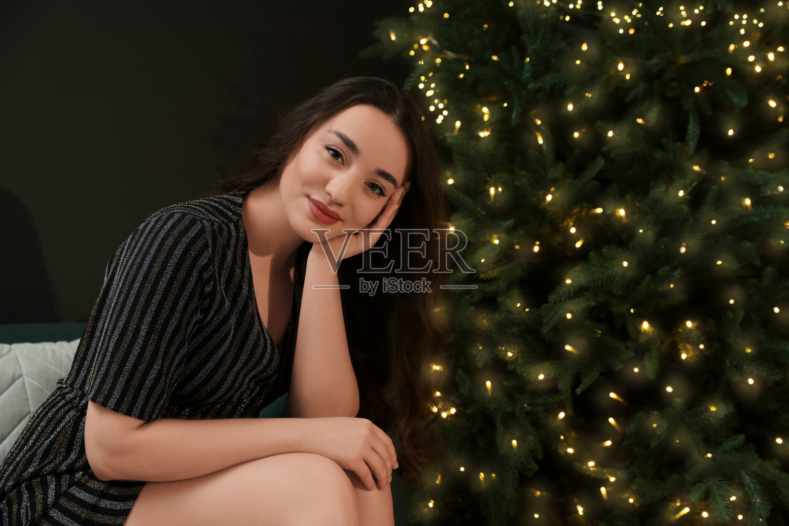 美丽的女人站在室内挂着金色彩灯的圣诞树旁照片摄影图片