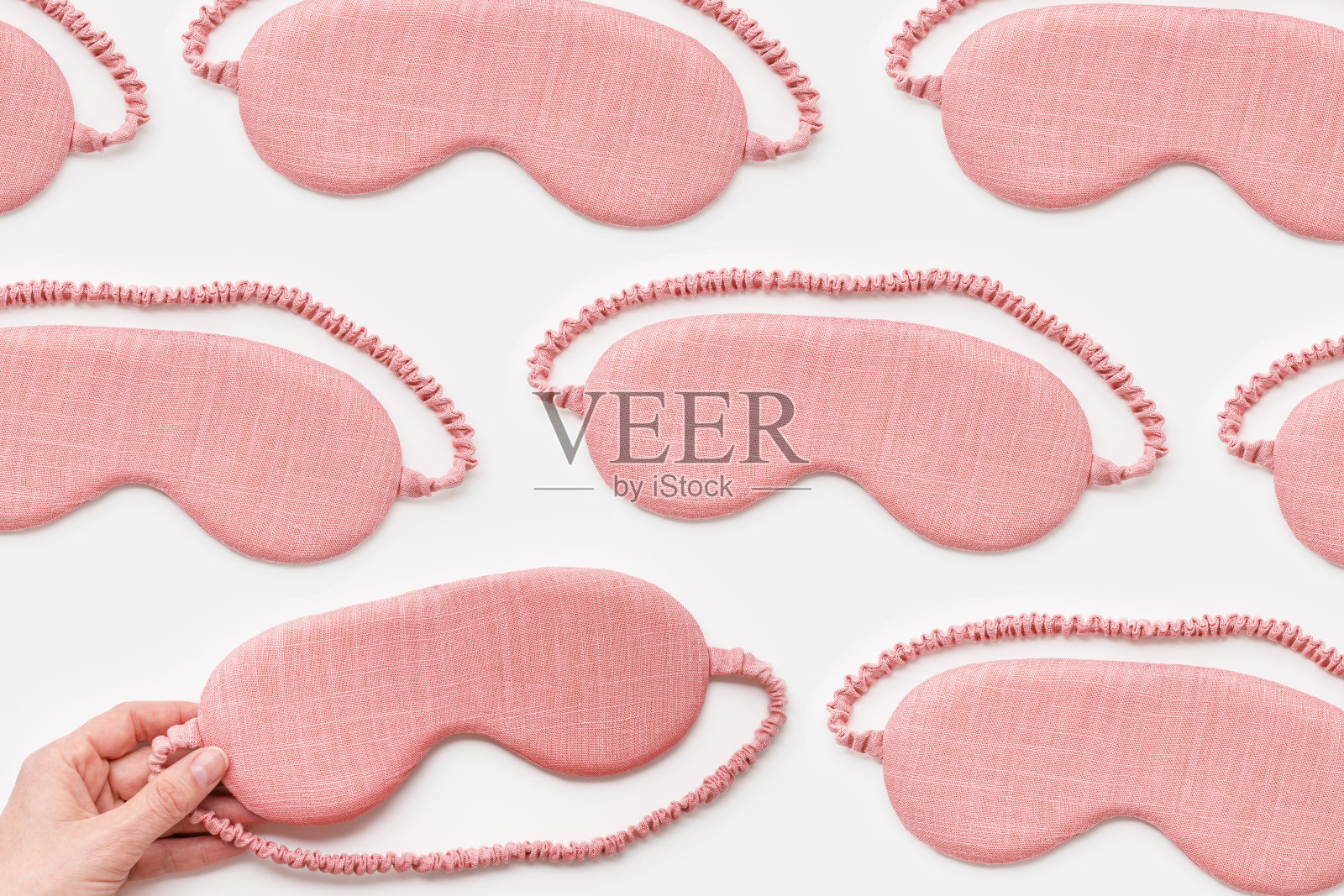 白色背景上睡眠面罩的最小图案。女性手持粉红眼罩，舒适休息，优质睡眠理念。软眼罩旅行，舒适休息，静物平躺照片摄影图片