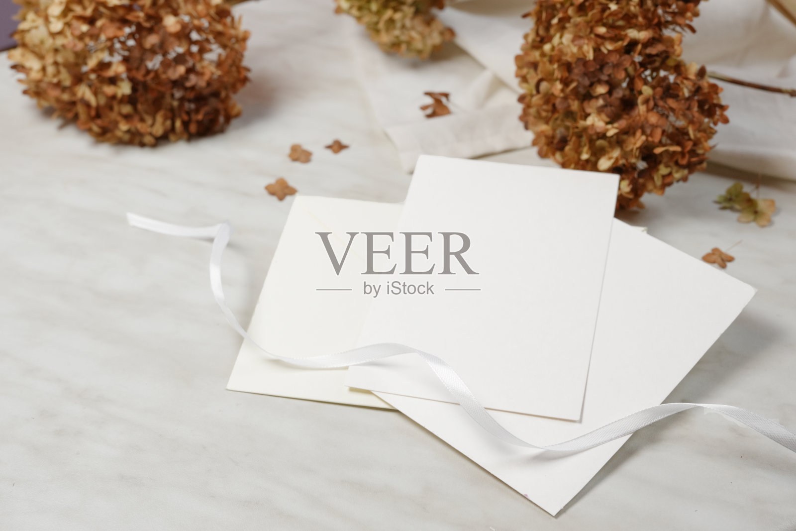 婚礼卡片模型与干绣球花在时尚的米色大理石背景。带有复制空间的侧视图。照片摄影图片