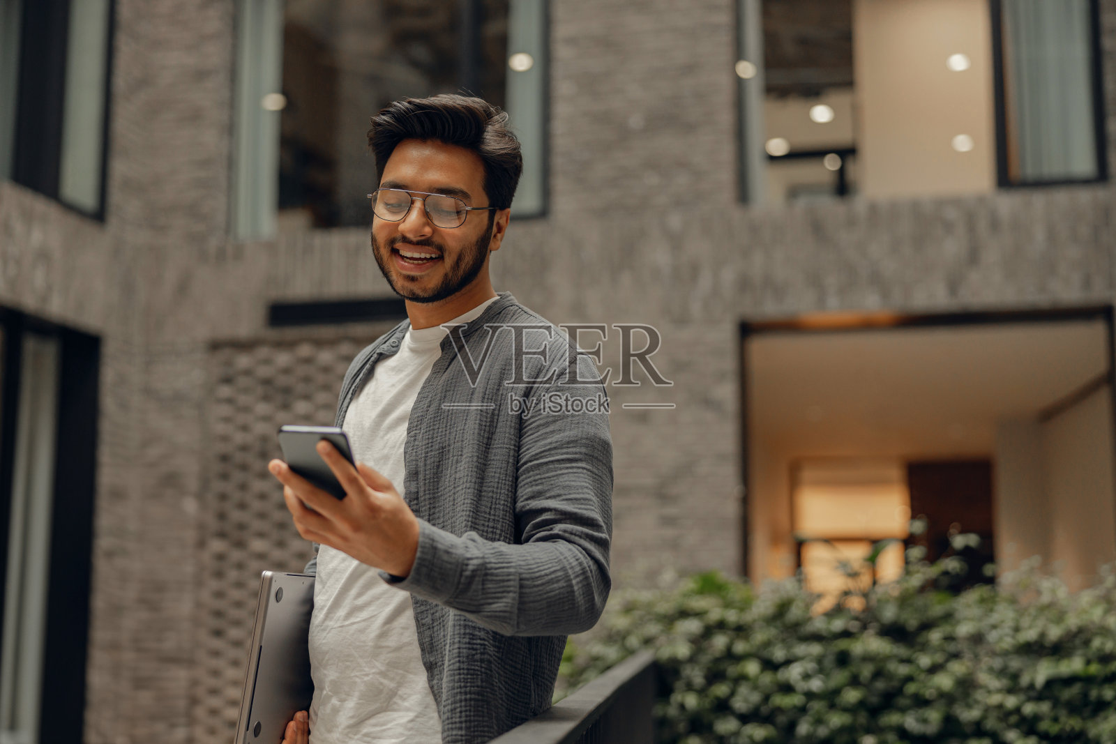 微笑的男性经理戴着眼镜站在现代的联合办公空间看手机照片摄影图片