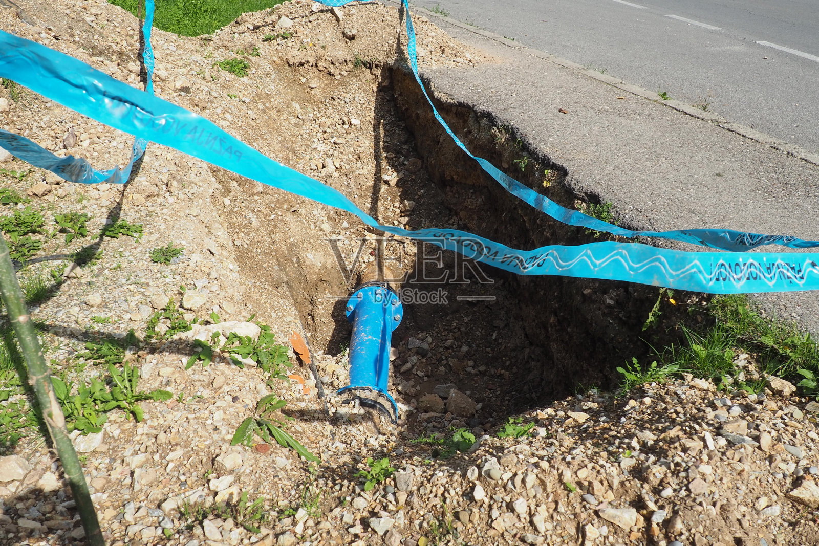 破碎的地面，洞。蓝色的水管。修复城市供水网络。塞尔维亚语的铭文——注意，管道。市政工程土方工程。折旧及摊销照片摄影图片