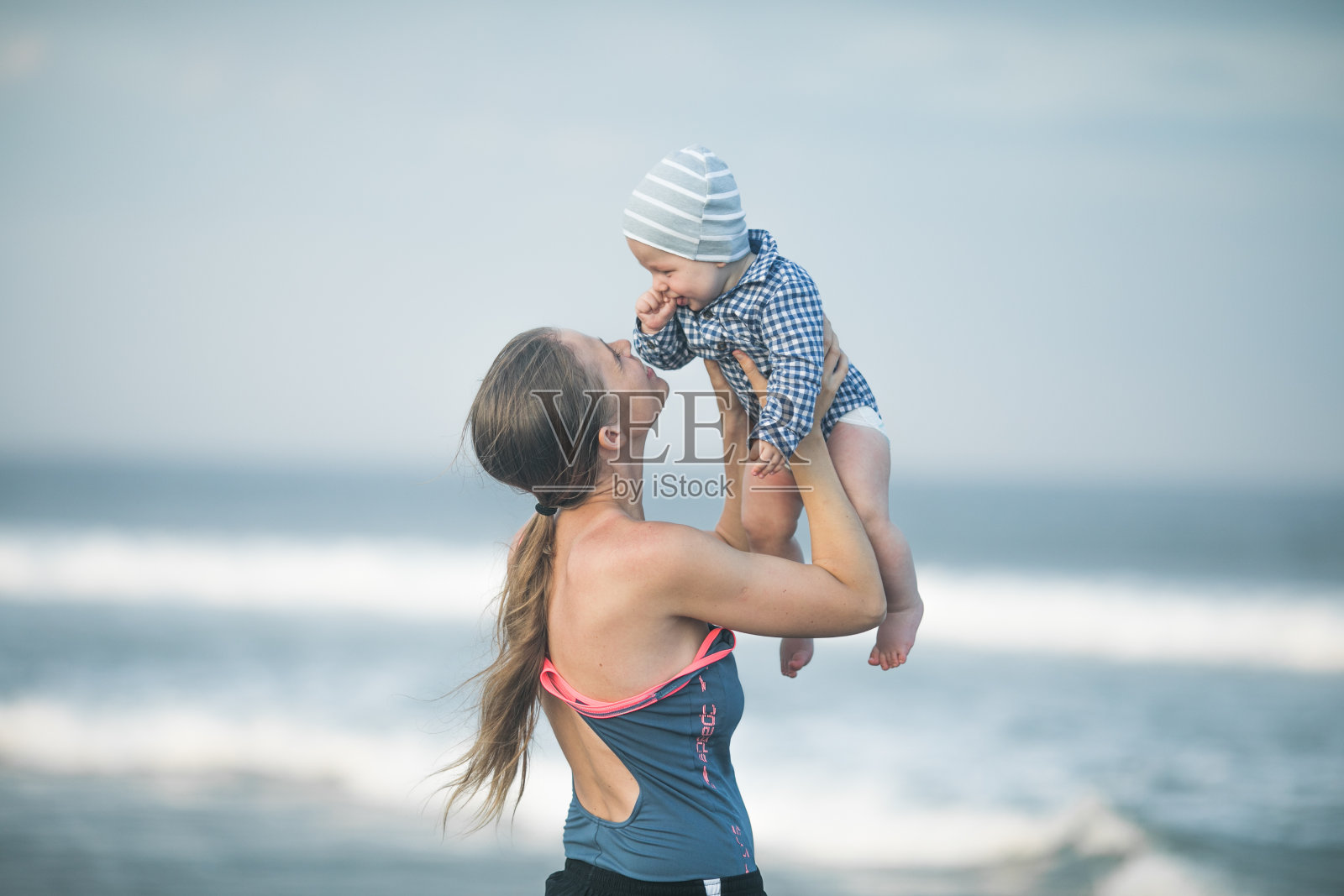 快乐的年轻母亲带着襁褓中的儿子在海边玩耍，父亲将孩子抛向空中照片摄影图片