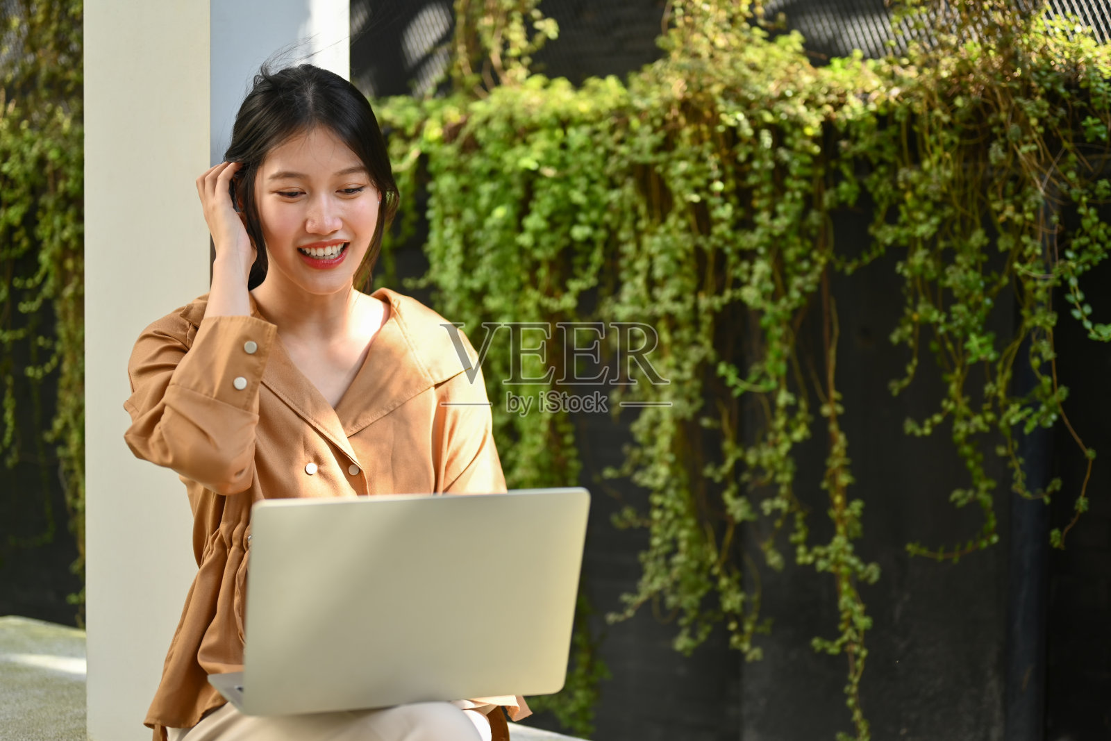 漂亮的年轻女子坐在办公大楼外的长凳上用笔记本电脑工作照片摄影图片