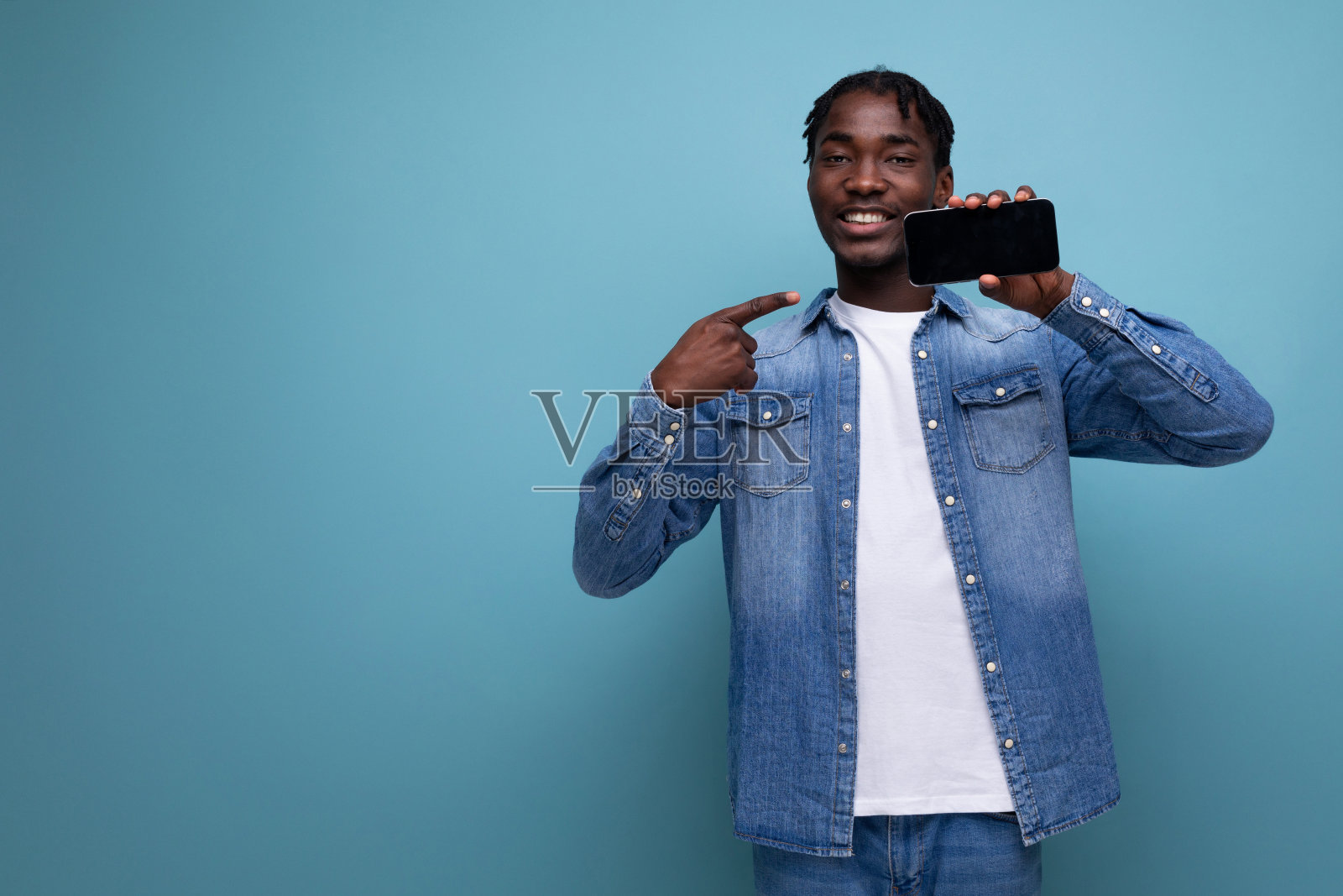 一头非洲卷发的时尚非洲男子展示了蓝色背景的智能手机模型，并带有复制空间照片摄影图片