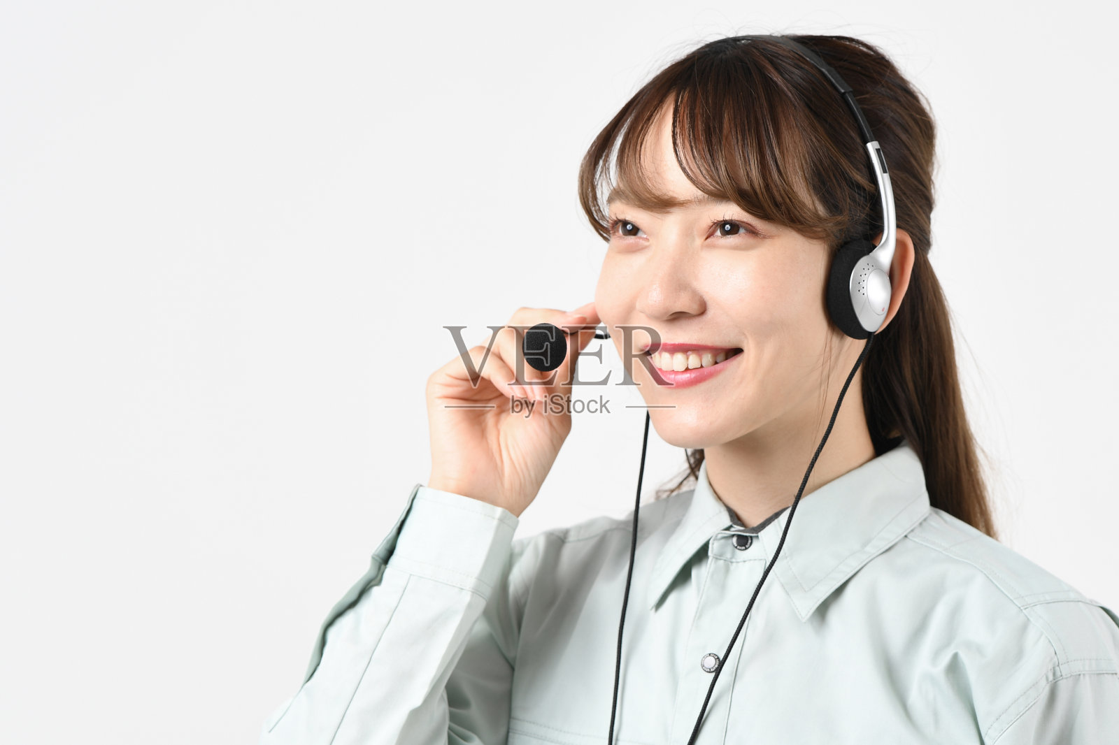 一位年轻的亚洲女性穿着工作服，戴着耳机，对着麦克风说话照片摄影图片