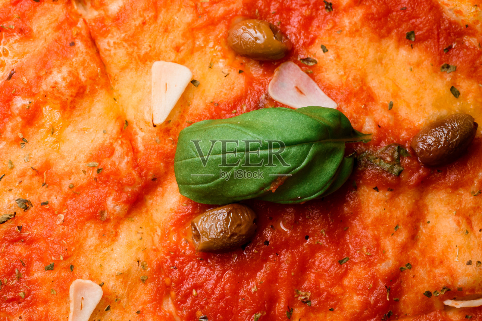 新鲜出炉的意大利披萨，配以番茄酱、罗勒、大蒜片、香草和绿橄榄。照片摄影图片