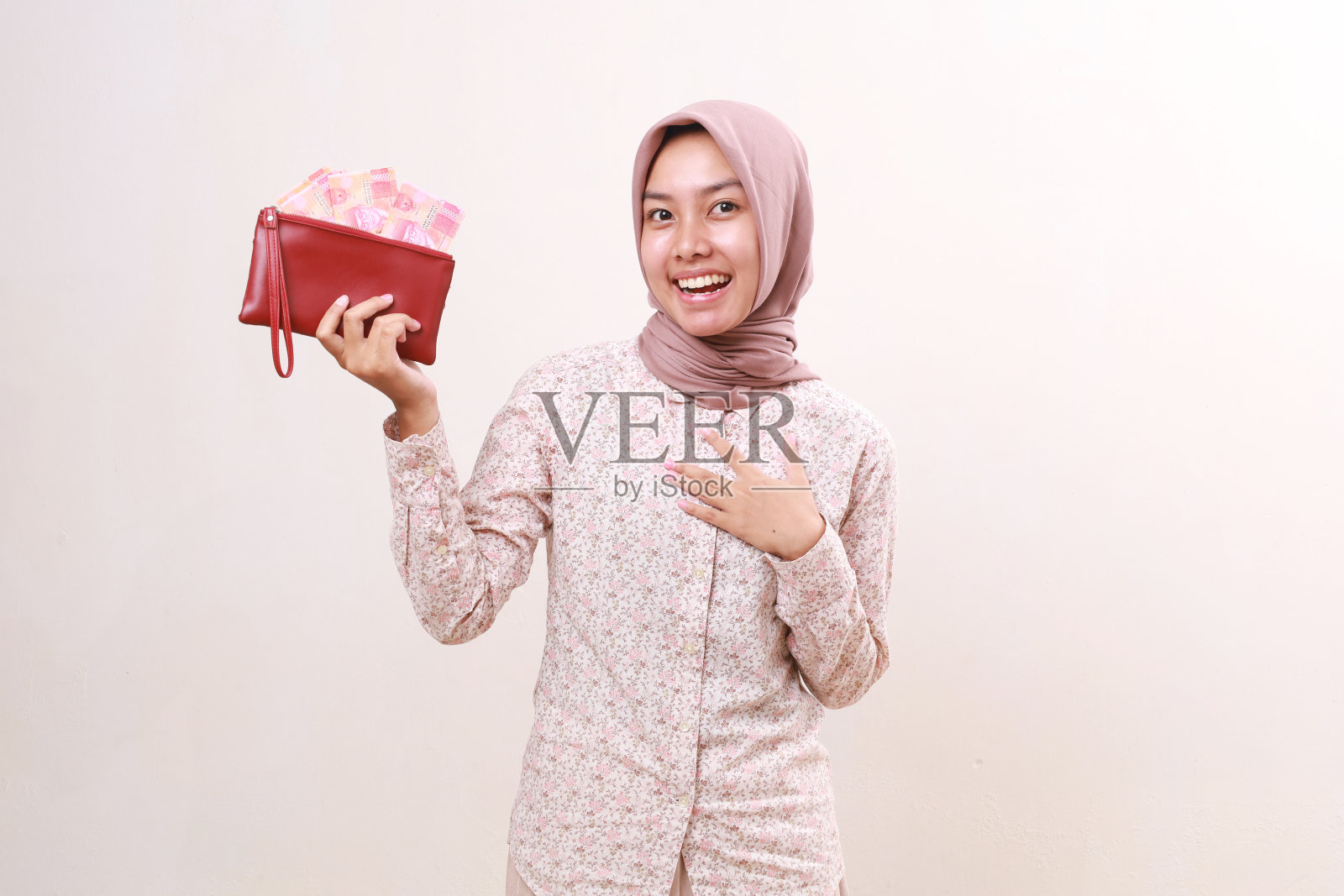 哇，兴奋的年轻亚洲穆斯林女子站在镜头前，手里拿着印尼钞票。隔离在白色背景上照片摄影图片