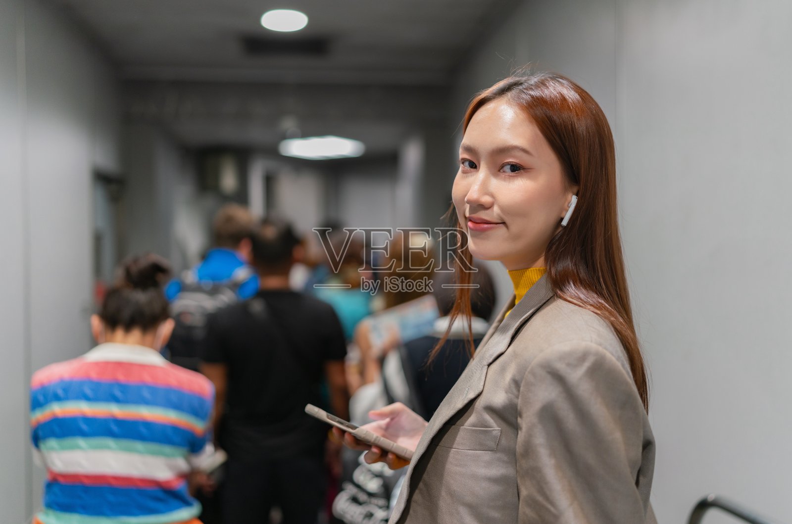 年轻的亚洲女子在机场的喷气桥，拿着智能手机，享受音乐，等待登机照片摄影图片