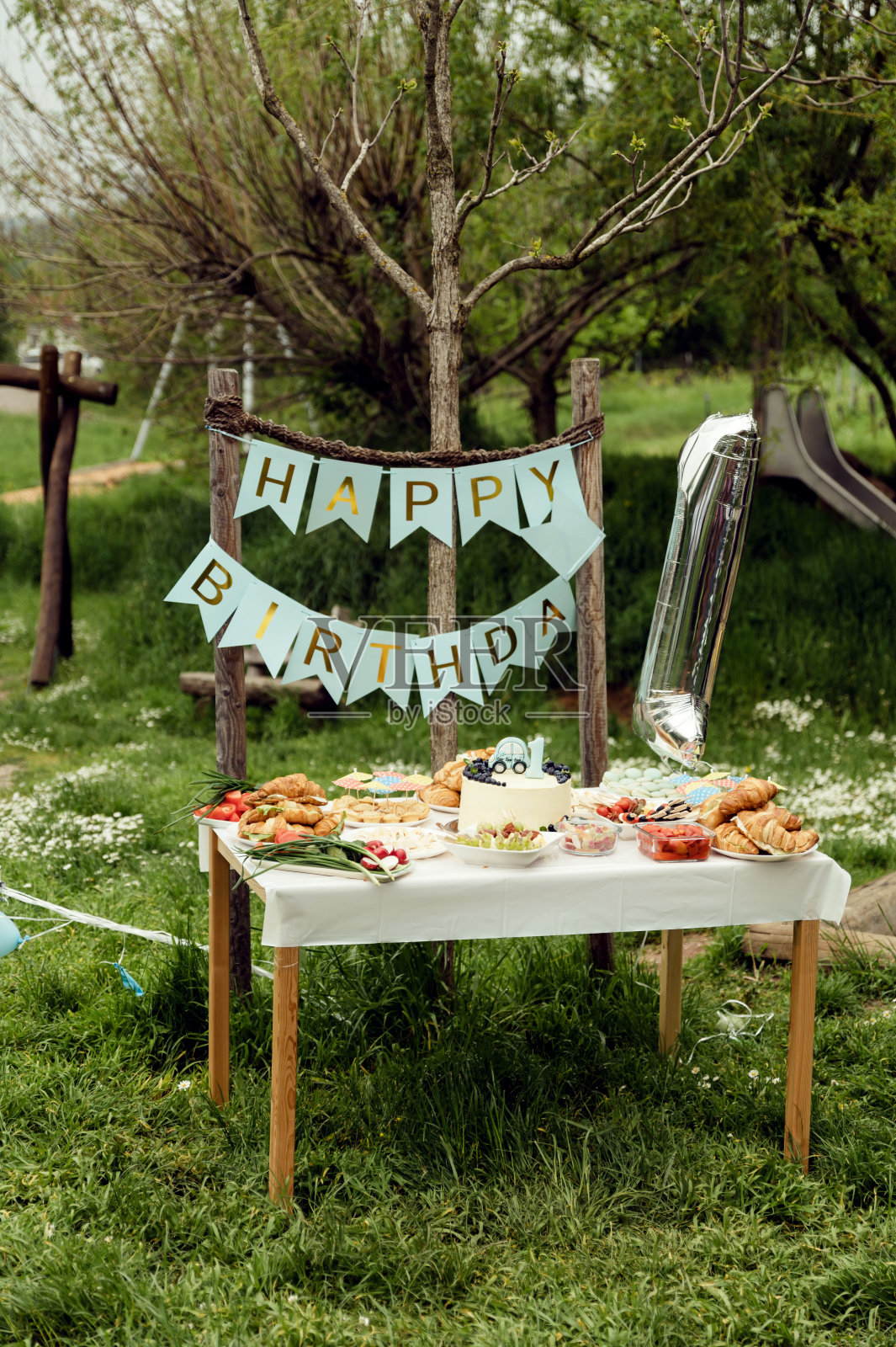 第一个生日的宴会。题词，生日快乐。节日餐桌配有食物和小吃，节日餐桌，以乡村风格为理念，在大自然中野餐庆祝生日照片摄影图片
