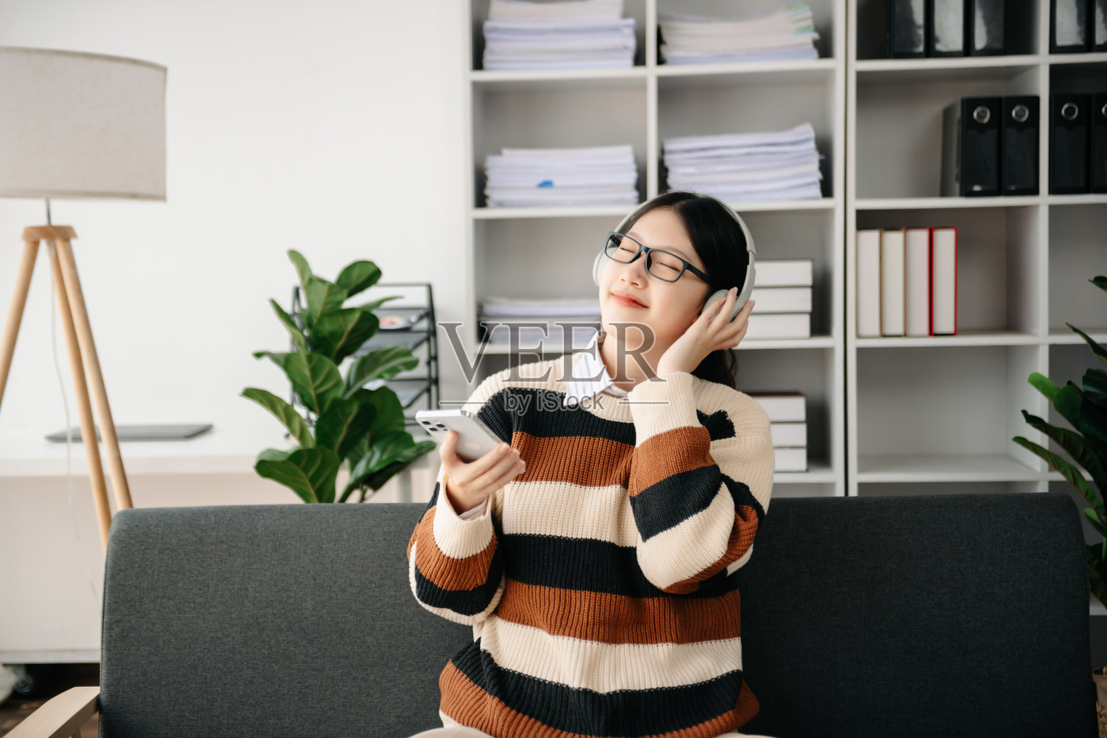 微笑的女孩在家里放松，她正在用智能手机平板电脑播放音乐，戴着白色耳机。沙发上照片摄影图片