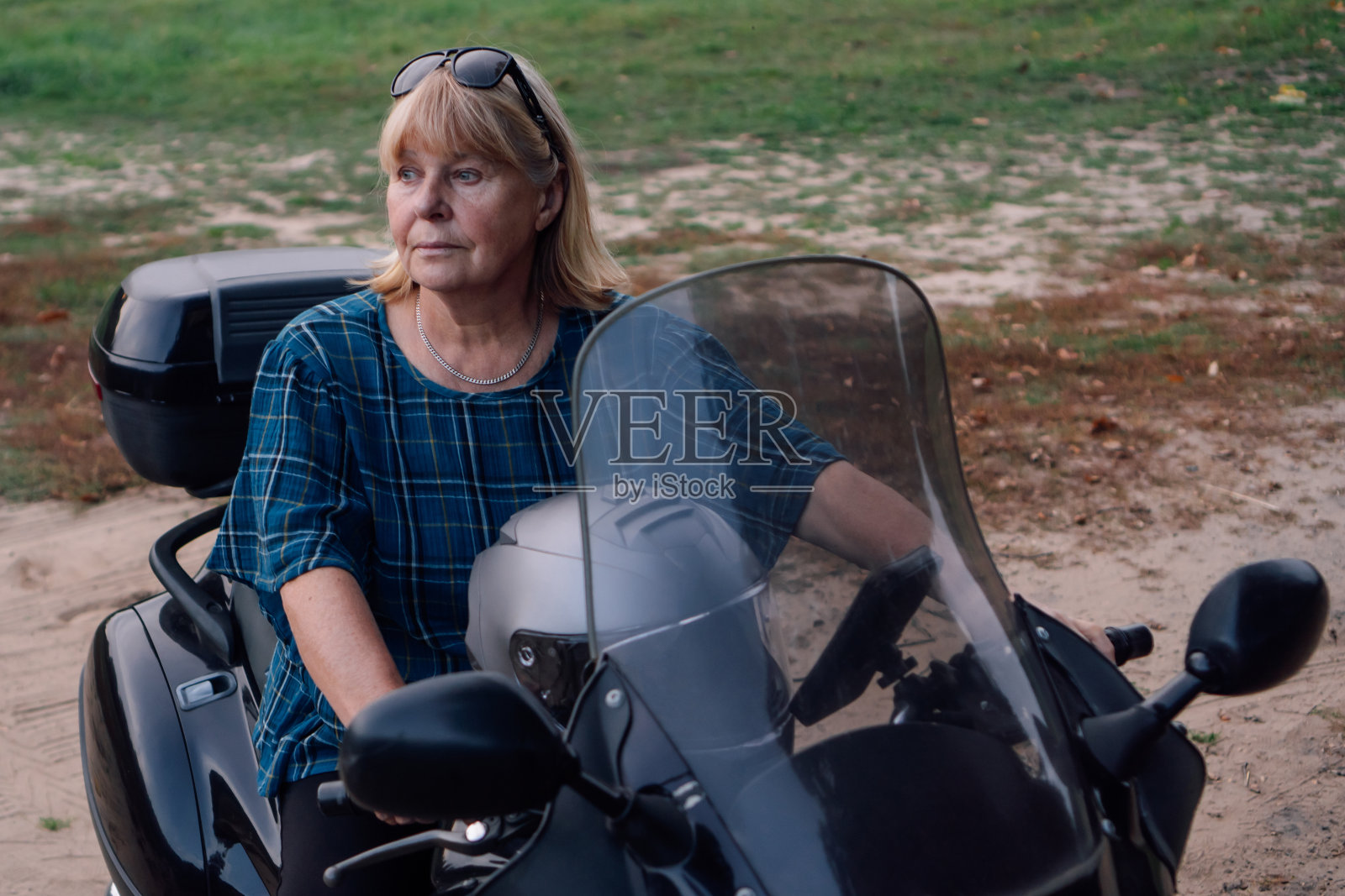 坚强独立成熟的金发女郎坐在摩托车上认真地看着旁边的秋天。照片摄影图片