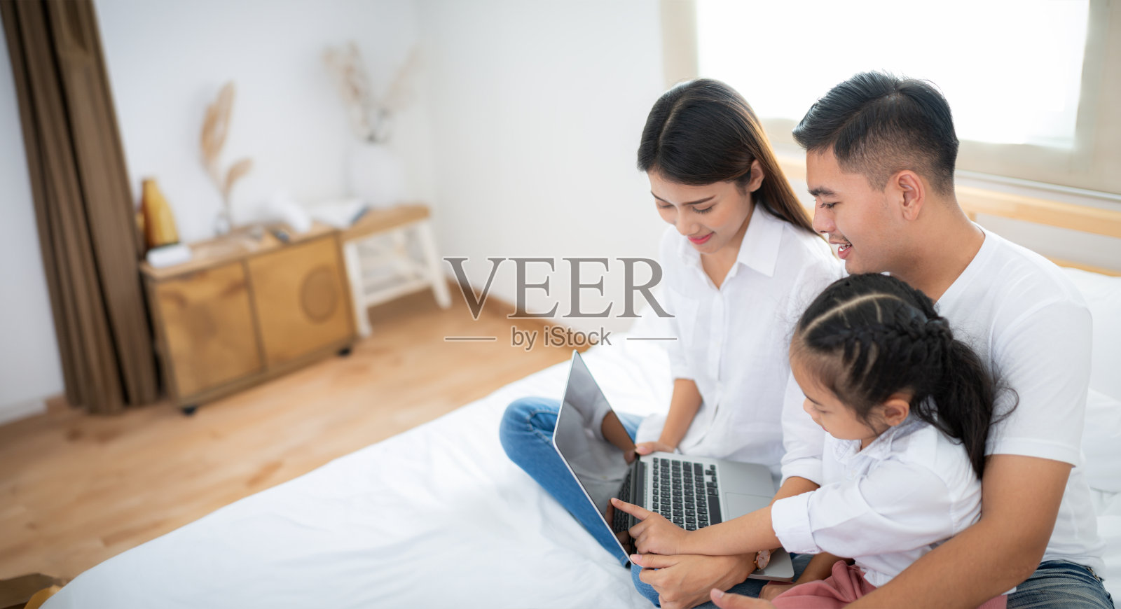 父亲和母亲带着女儿在床上放松地使用笔记本电脑。照片摄影图片