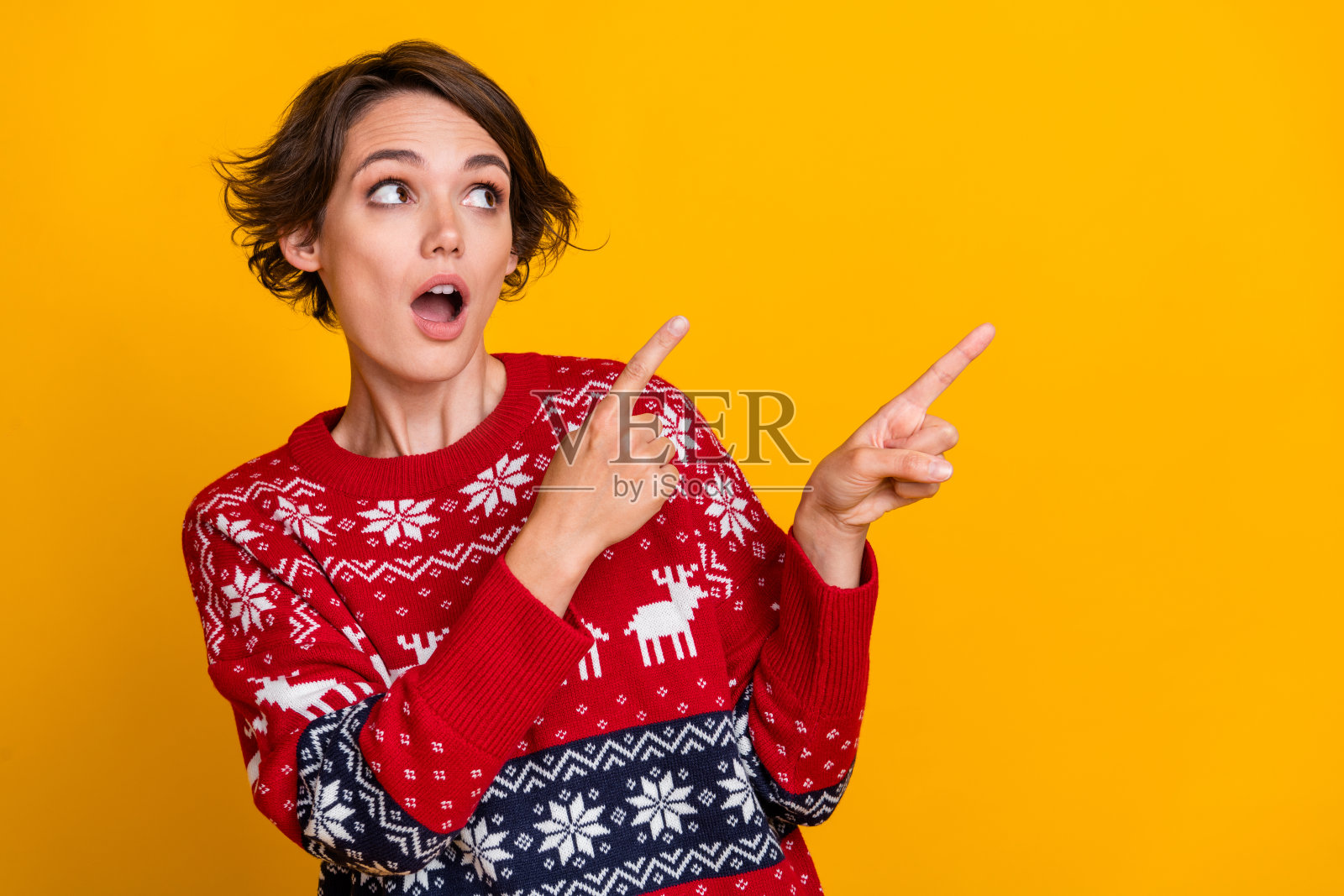 印象深刻的女人的肖像，时尚的发型，穿着毛衣，表明凝视着黄色背景上孤立的空白空间照片摄影图片