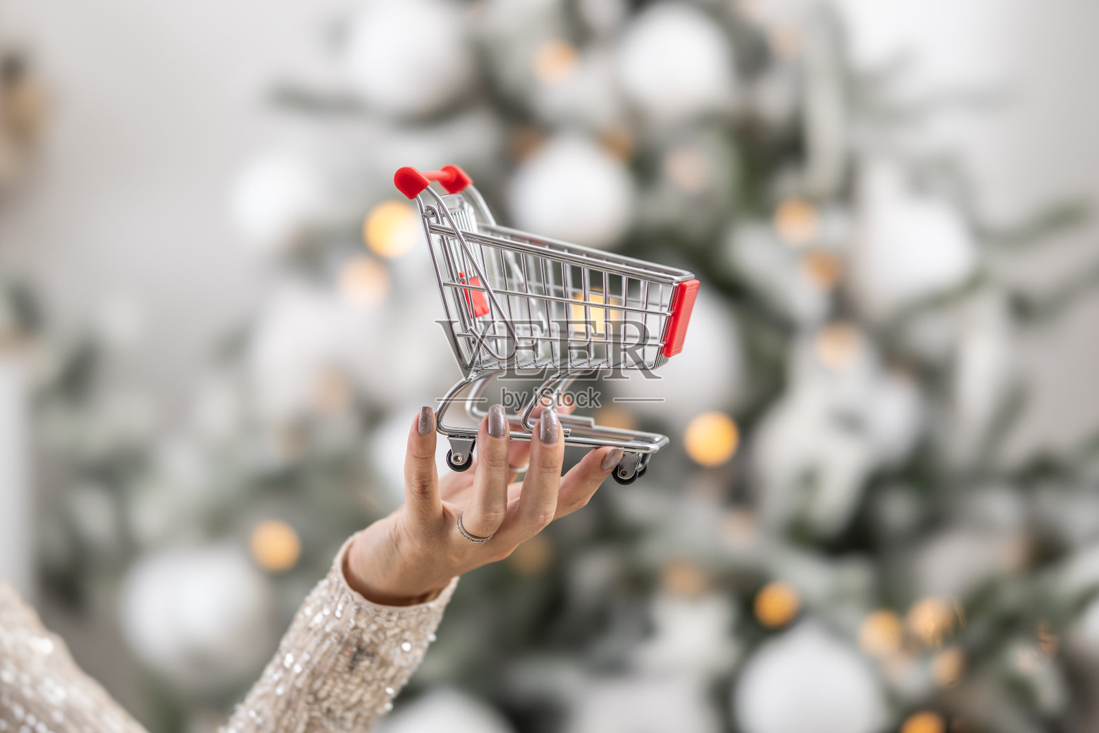女性手持小购物车作为圣诞购物期的象征。照片摄影图片