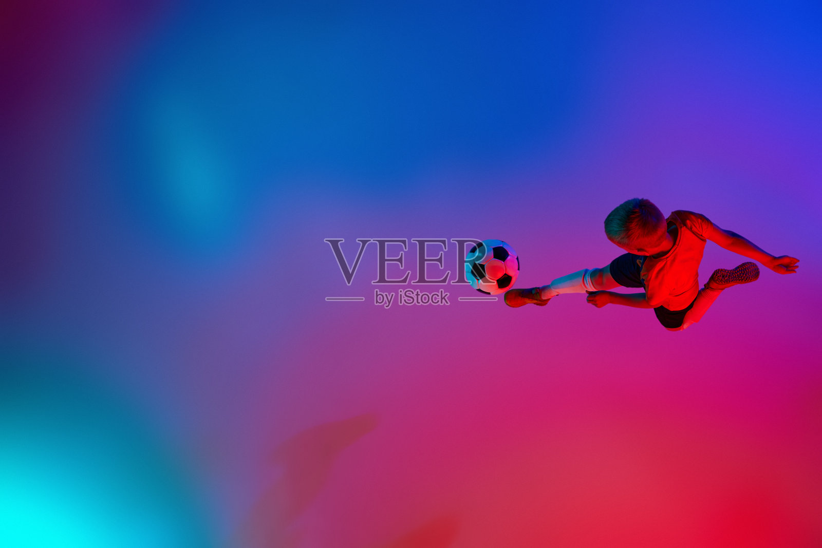在渐变的红蓝霓虹灯下，小男孩在训练中玩足球的鸟瞰图。运动理念，运动生活方式，团队游戏，健康，活力照片摄影图片