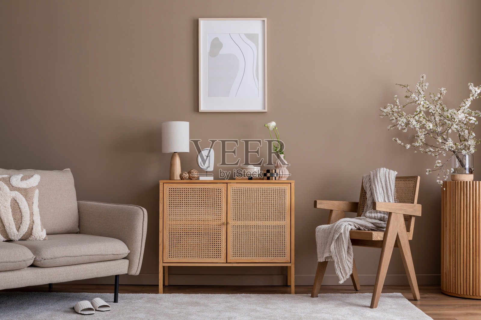 温馨舒适的客厅内部，模拟海报框架，藤餐具柜，木制扶手椅，米色沙发，明亮的地毯，格纹，樱花和个人配件。家居装饰。模板。照片摄影图片