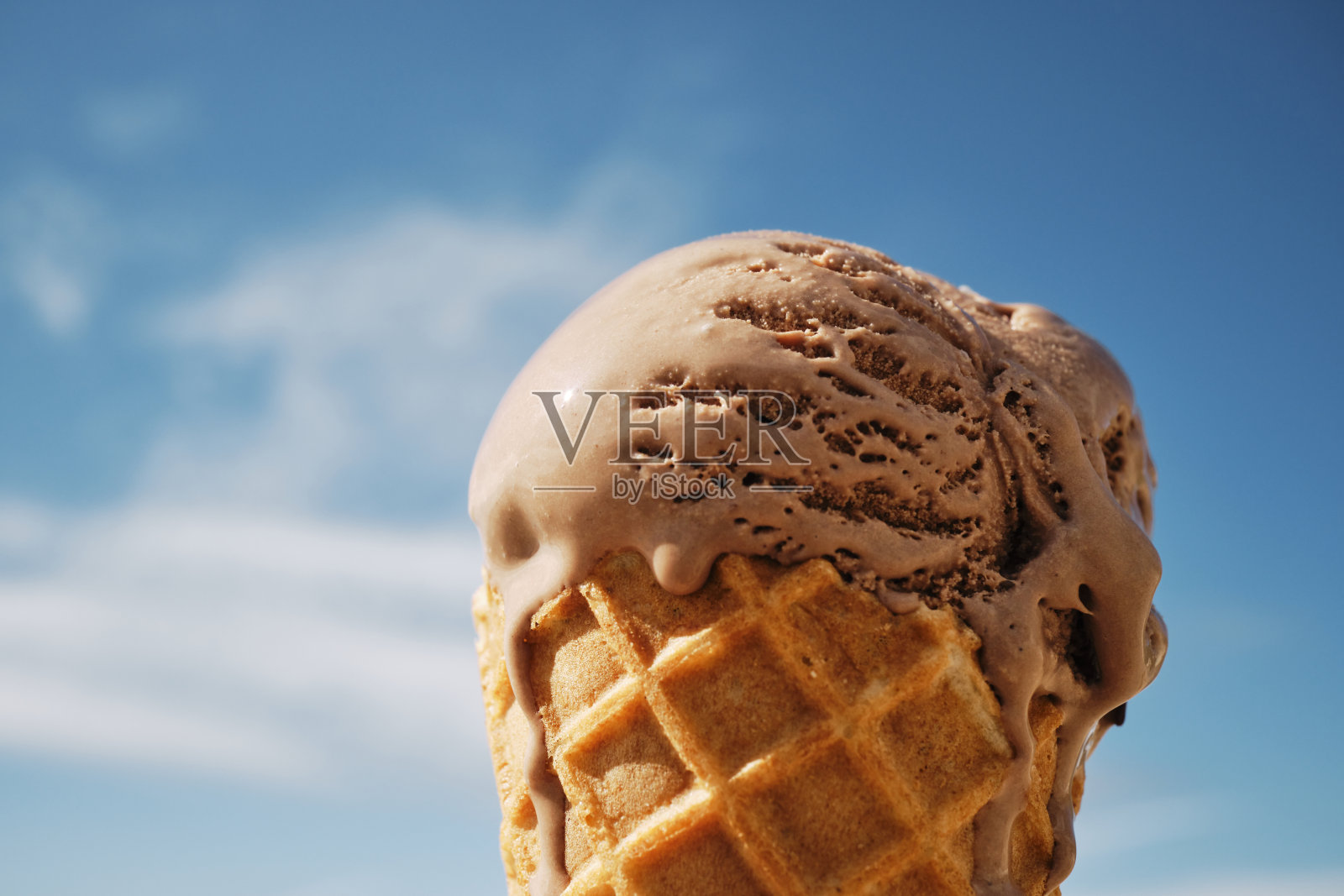 夏日蔚蓝的天空映衬着正在融化的巧克力甜筒。照片摄影图片