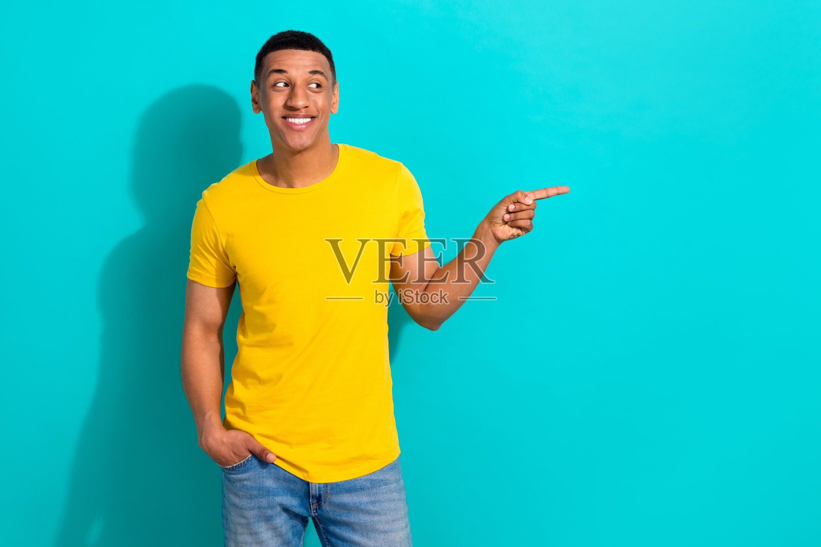 照片上有思想的积极的家伙穿着黄色的t恤，看起来手指空白，孤立的蓝绿色背景照片摄影图片