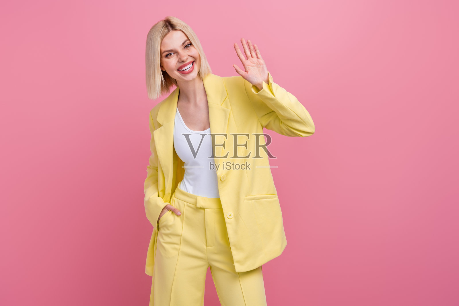 照片积极友好的女士穿着黄色夹克西装微笑挥舞手臂hi孤立的粉红色背景照片摄影图片